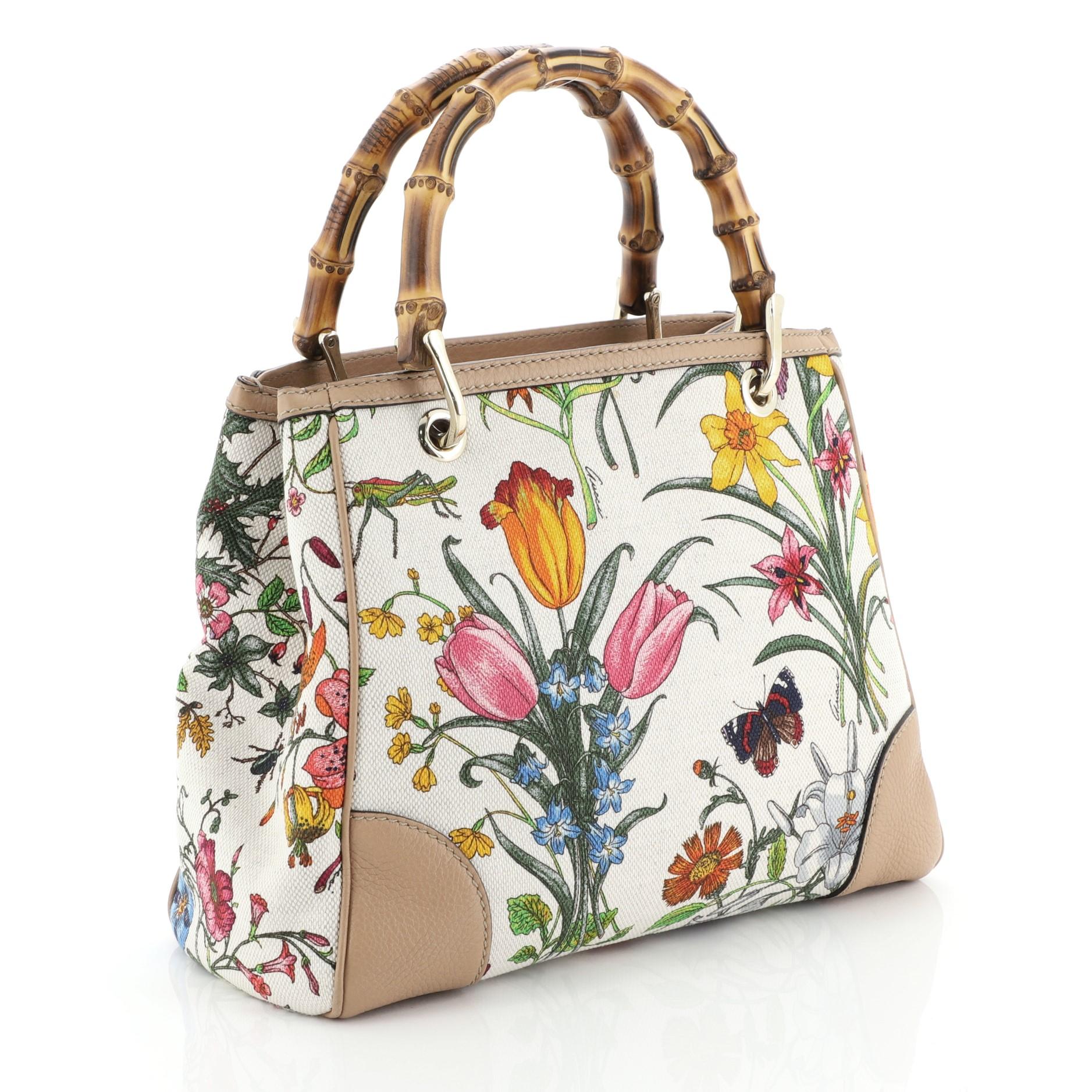 This Gucci Bamboo Shopper Tote Flora Canvas Small, crafted in white printed canvas, features dual bamboo handles and gold-tone hardware. Its hidden magnetic snap closure opens to a neutral fabric interior divided into two compartments with side zip
