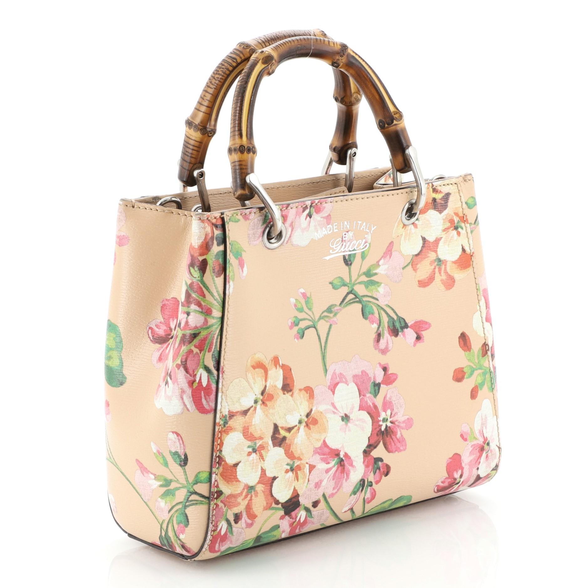 This Gucci Bamboo Shopper Tote Blooms Print Leather Mini, crafted from pink blooms printed leather, features sturdy bamboo handles, stamped logo at the front, and silver-tone hardware. Its hidden magnetic snap closure opens to a neutral fabric