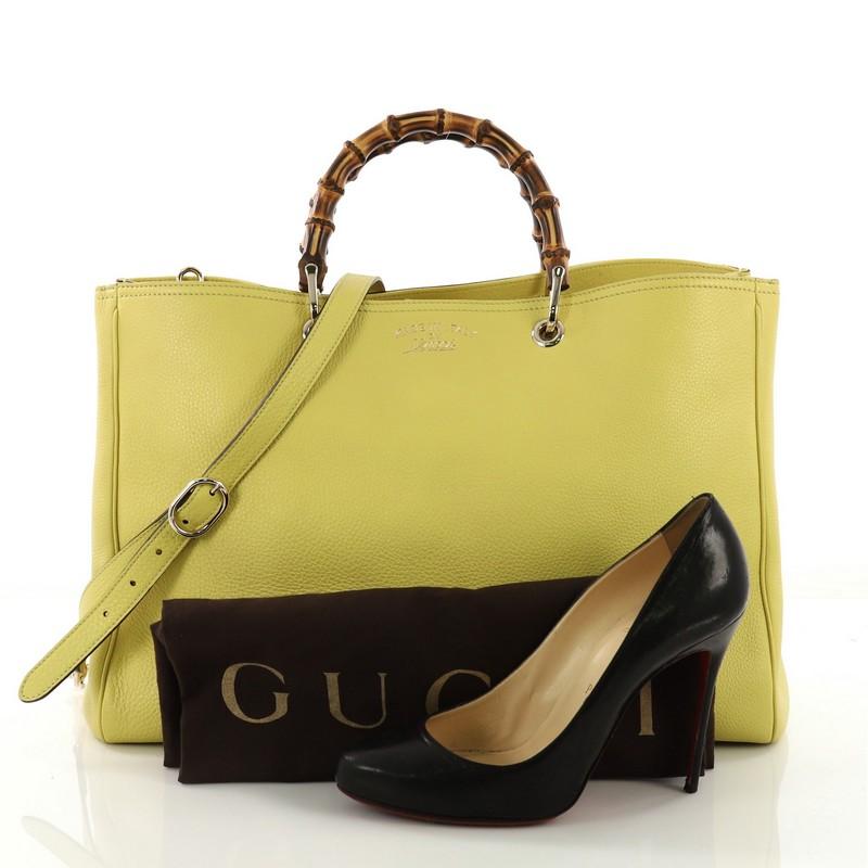 This Gucci Bamboo Shopper Tote Leather Large, crafted from yellow leather, features sturdy bamboo handles, stamped logo at the front, and gold-tone hardware. Its hidden magnetic snap closure opens to a beige canvas interior with middle zip and main