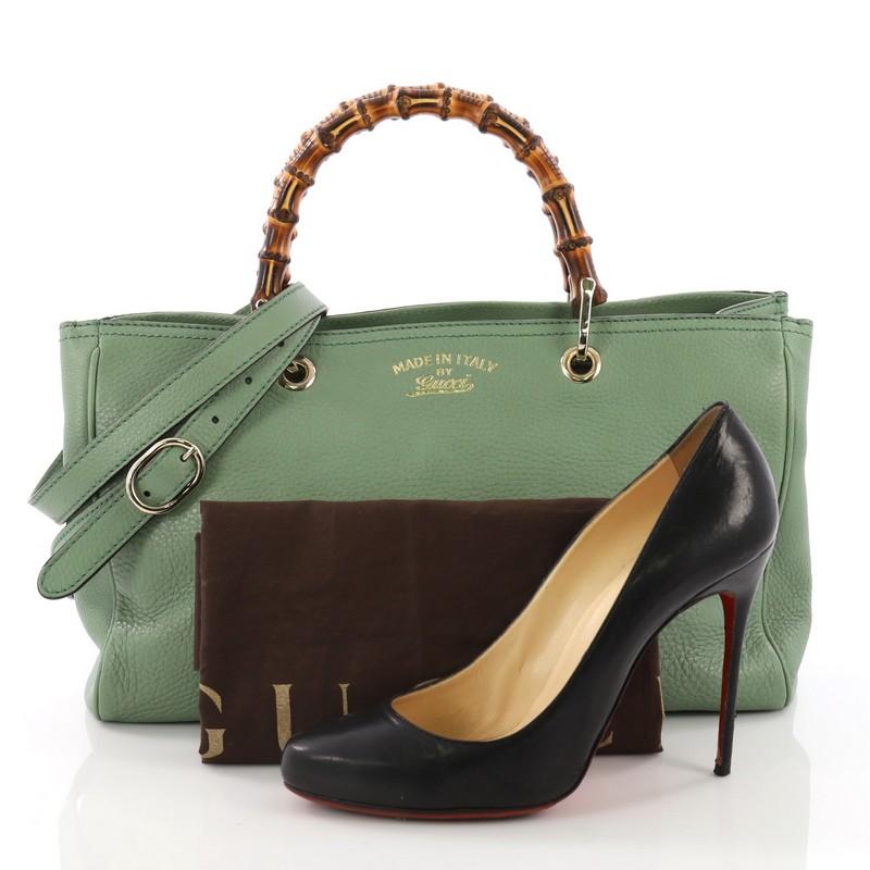 This Gucci Bamboo Shopper Tote Leather Medium, crafted in green leather, features sturdy bamboo handles, protective base studs, and gold-tone hardware. Its hidden magnetic snap closure opens to a beige canvas interior divided into two compartments