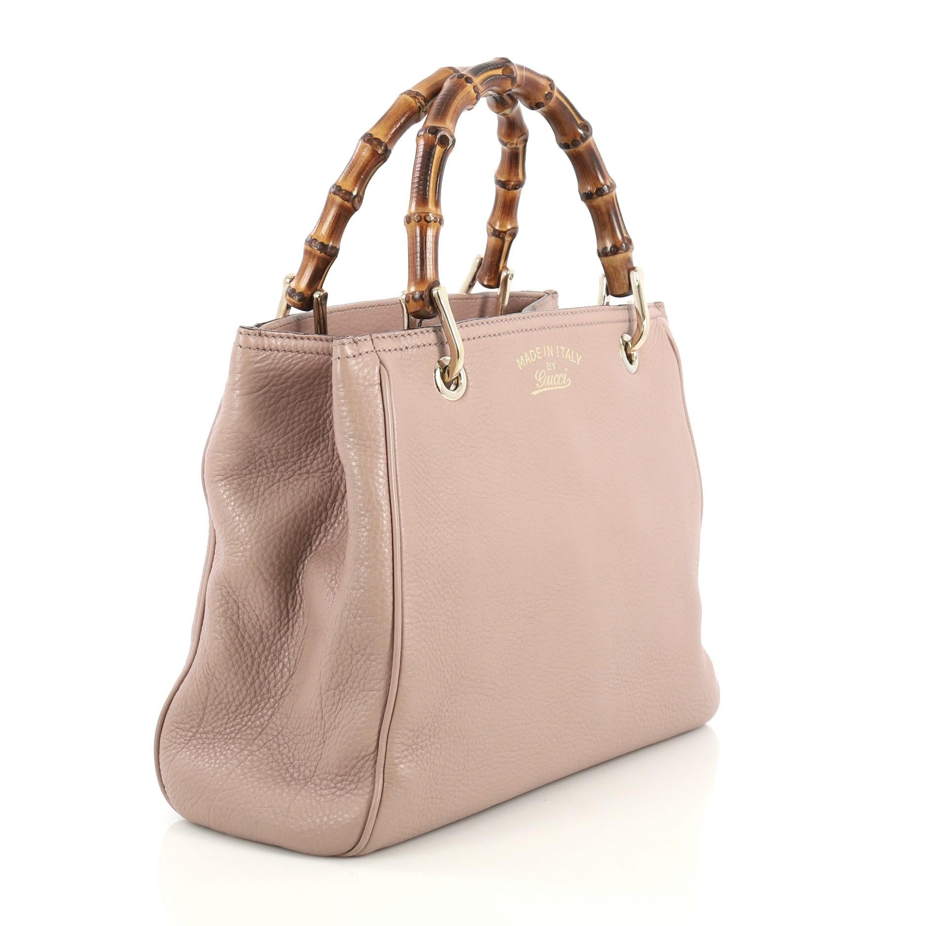 This Gucci Bamboo Shopper Tote Leather Small, crafted in neutral leather, features dual bamboo handles, protective base studs, and gold-tone hardware. Its hidden magnetic snap closure opens to a neutral fabric interior divided into two compartments