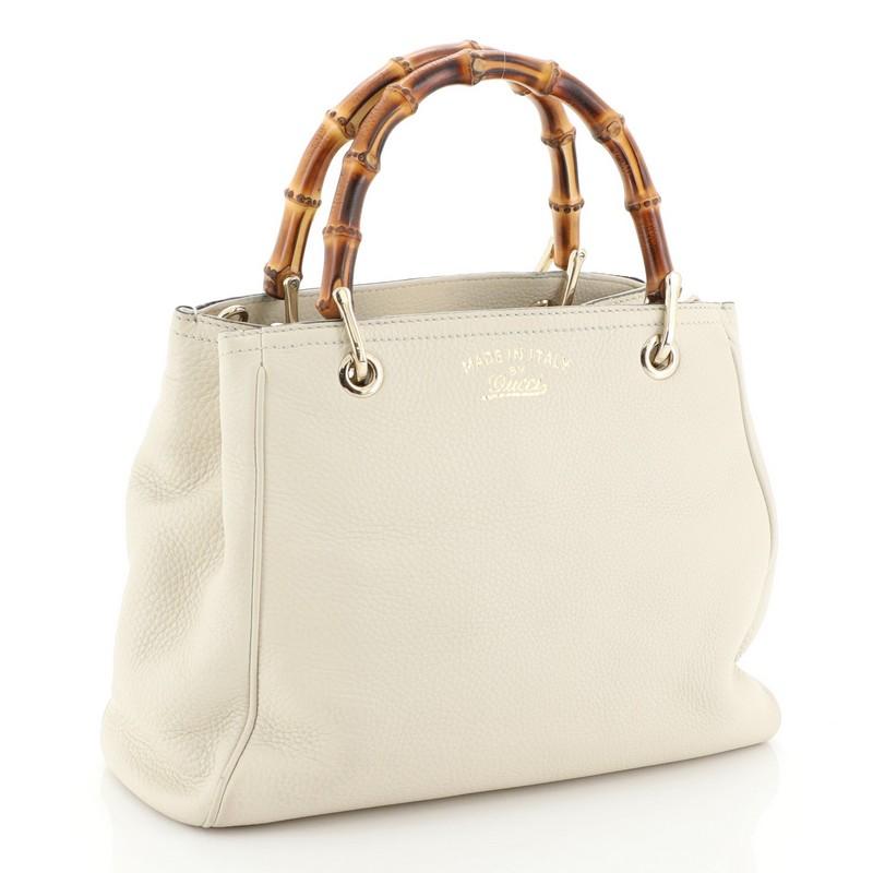 This Gucci Bamboo Shopper Tote Leather Small, crafted in neutral leather, features dual bamboo handles, protective base studs, and gold-tone hardware. Its hidden magnetic snap closure opens to a neutral fabric interior divided into two compartments