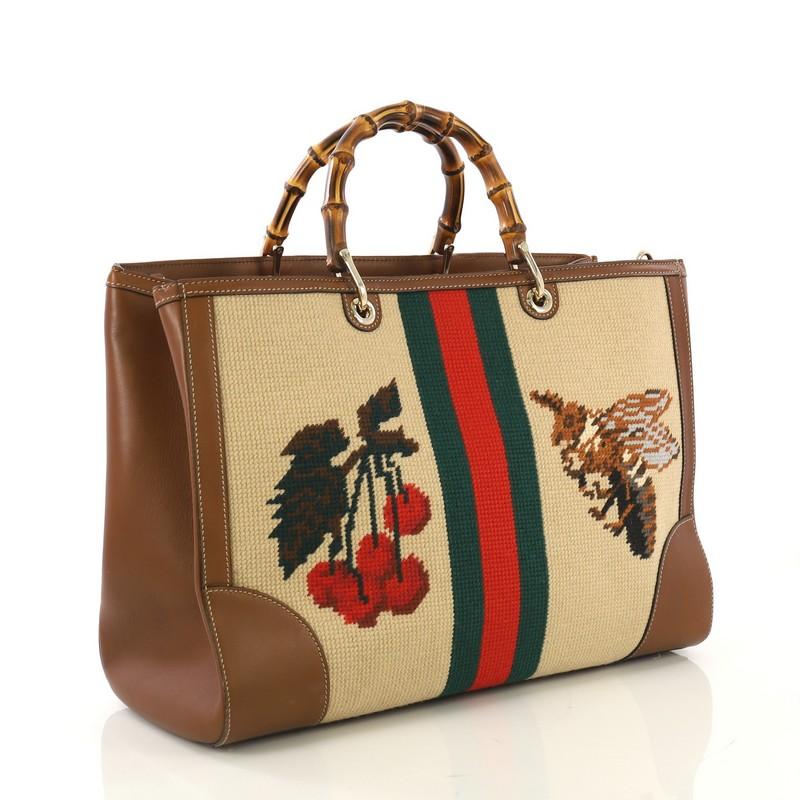This Gucci Bamboo Shopper Tote Needle Point Textile Large, crafted from brown needle point textile and brown leather, features bamboo handles, embroidered lion on one side, bee and cherries with web stripe on opposite side, protective base studs,