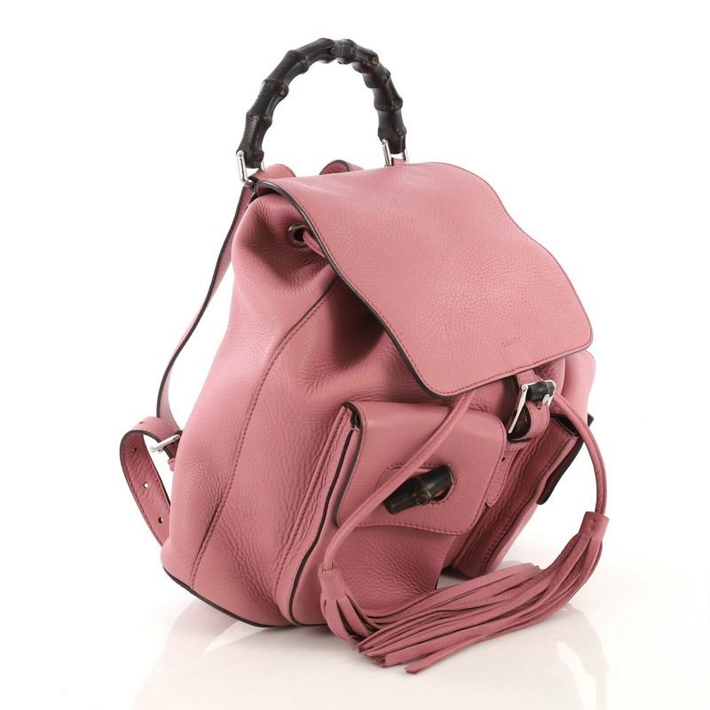 This Gucci Bamboo Tassel Backpack Leather Medium, crafted from pink leather, features bamboo top handle, adjustable leather straps, two exterior pockets with bamboo closure, hanging leather tassels, and silver-tone hardware. Its buckle and