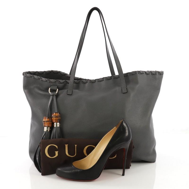 This Gucci Bamboo Tassel Tote Leather Large, crafted in gray leather, features dual flat leather handles, whipstitched detailing, and gold-tone hardware. Its magnetic closure opens to a brown fabric interior slip pockets. **Note: Shoe photographed