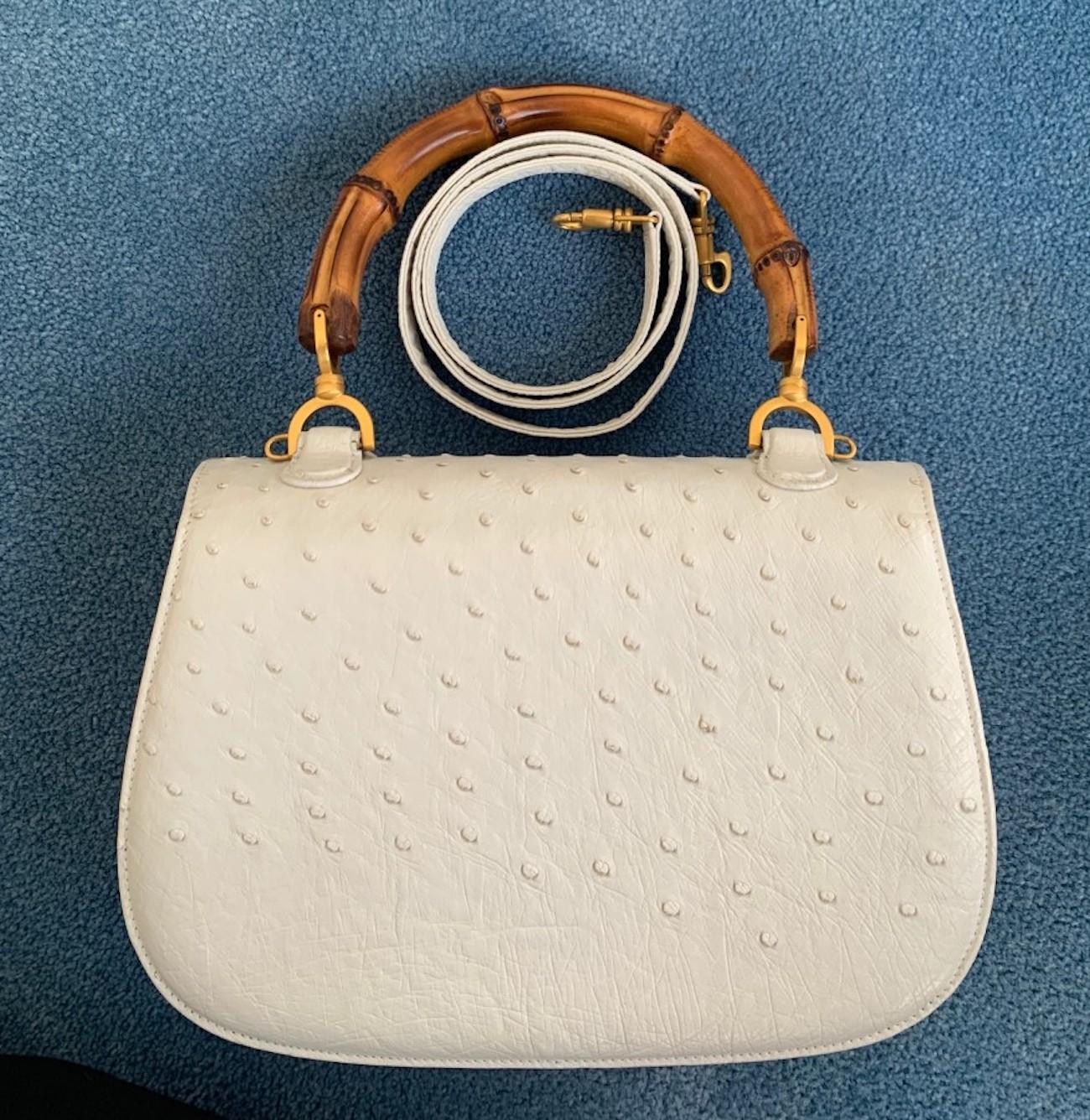Presented here is the classic Gucci top handle bamboo hand bag in white ostrich leather. It has a structured brown bamboo top handle and detachable shoulder strap . The bag also features a fold over top,  a matching bamboo twist-lock closure, an