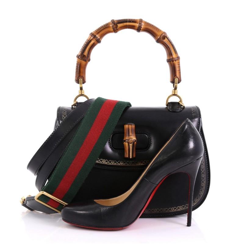 This Gucci Bamboo Web Top Handle Bag Printed Leather Small, crafted in black leathers, features a bamboo top handle, decorative golden frame print border, and gold-tone hardware. Its bamboo turn-lock closure opens to a printed fabric interior with