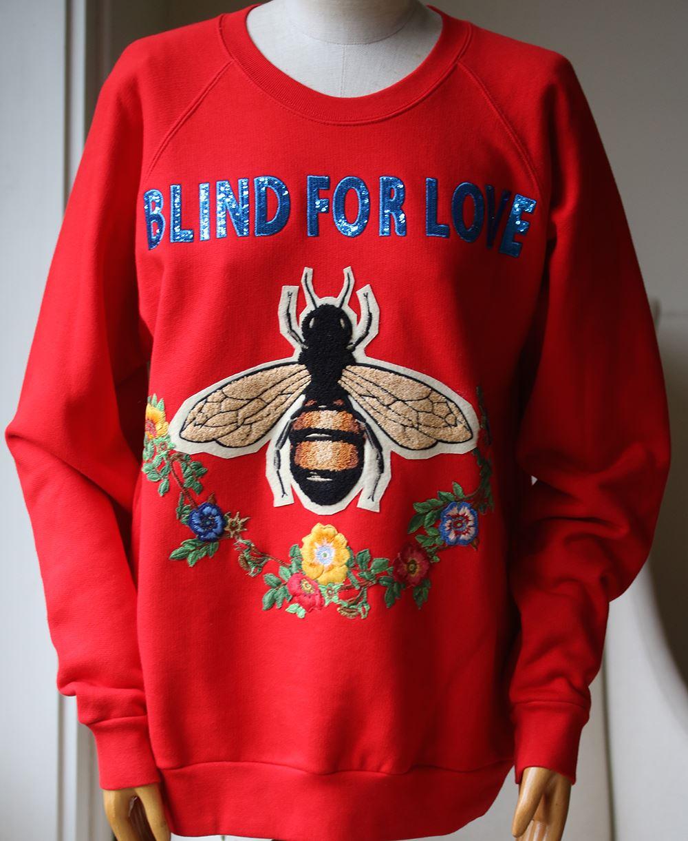 The sweatshirt, an essential cut carried season to season, features embroidered appliqués representing several symbolic Gucci motifs, including the bee surrounded by a garland of flowers. Blind for Love