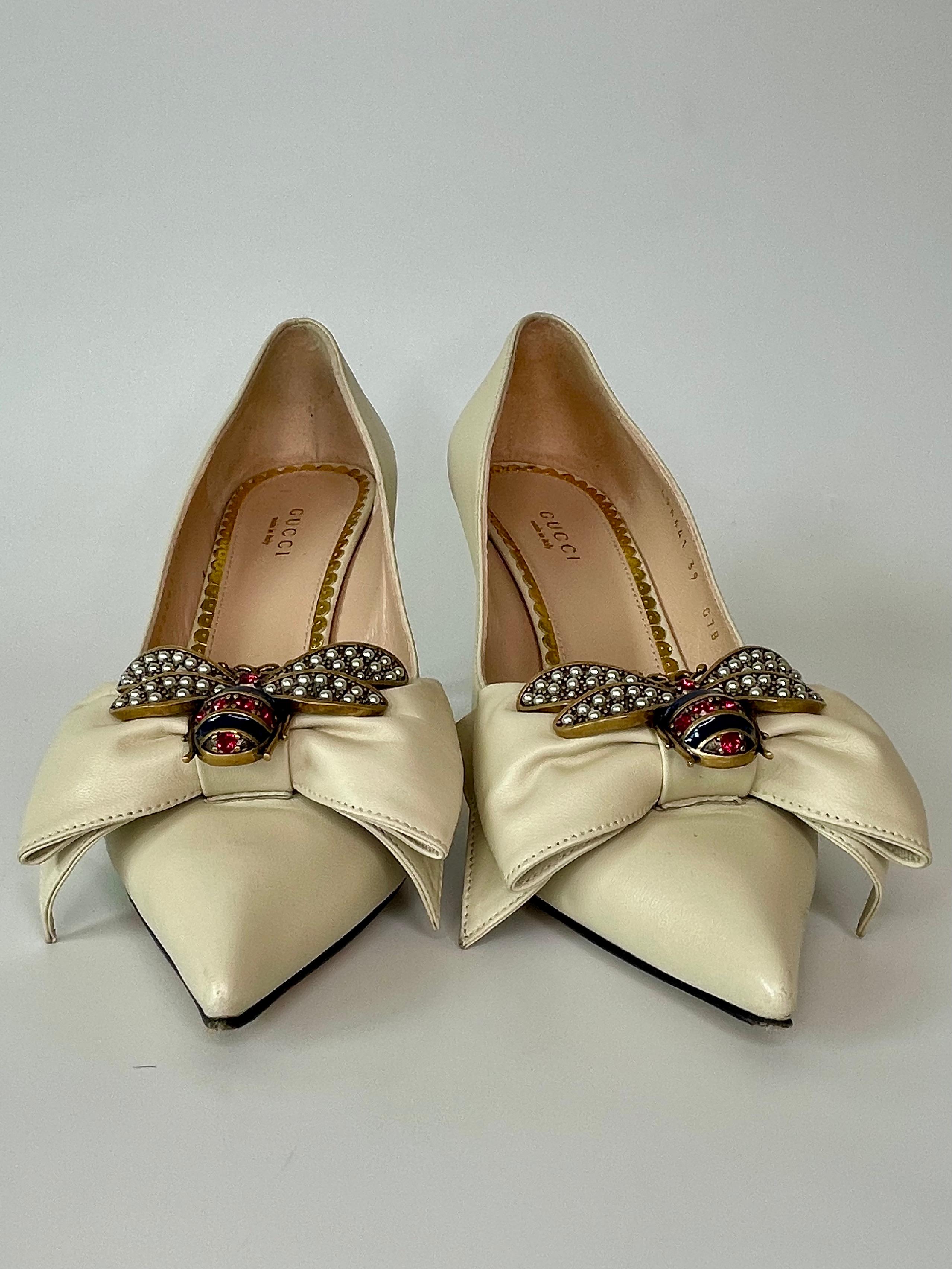 These Gucci pumps are made with cream leather and feature a pointed toe, heels measuring 3 inches and an oversize leather bow with a metallic bee detail embellishment at centre. The bee is encrusted with pearl effect studs and enamel
