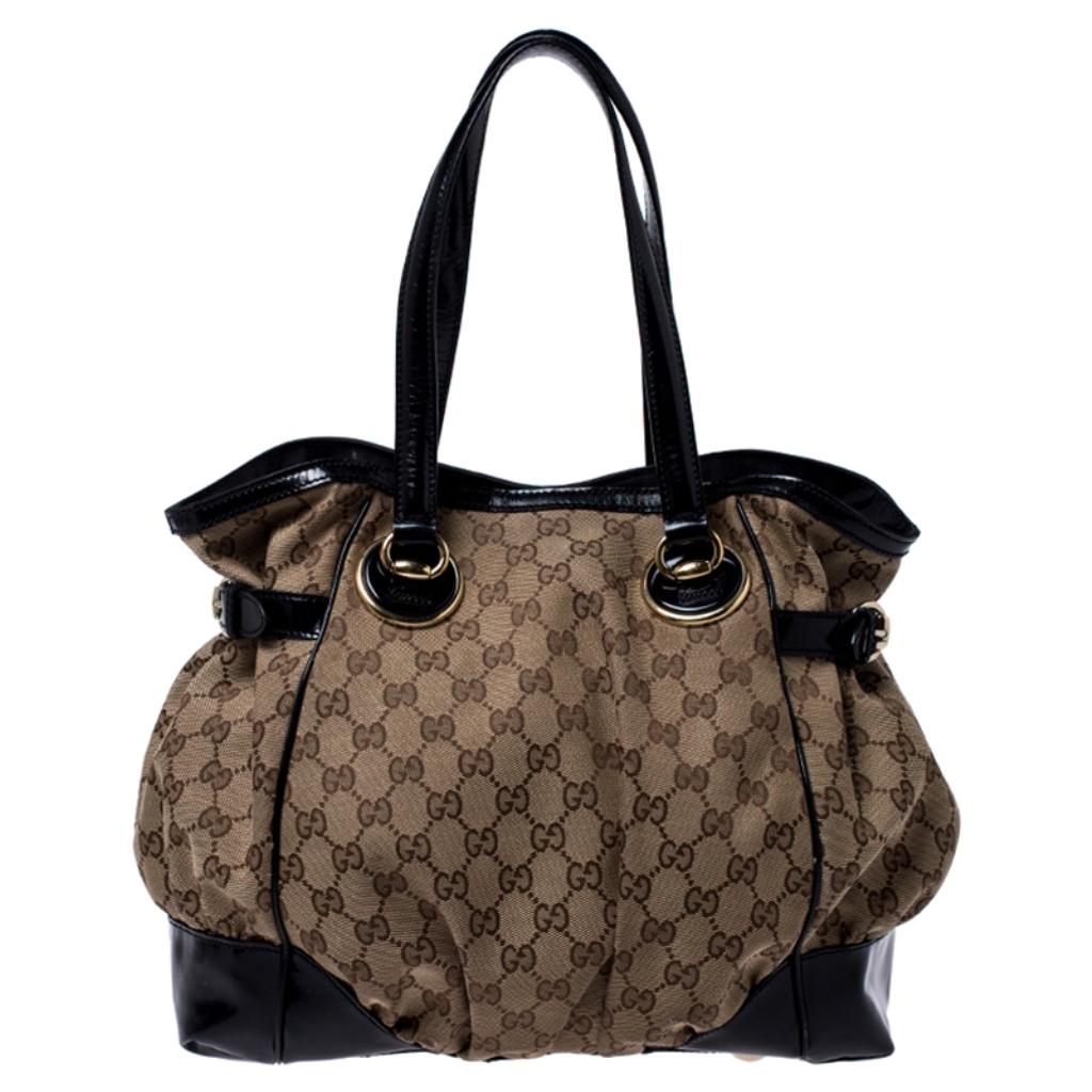 This Gucci Full Moon tote is a roomy and stylish bag that is perfect for everyday use. Crafted from signature beige GG canvas with black patent leather trims, the bag comes with top flat handles, buckle belts on the sides and studded bottom. The