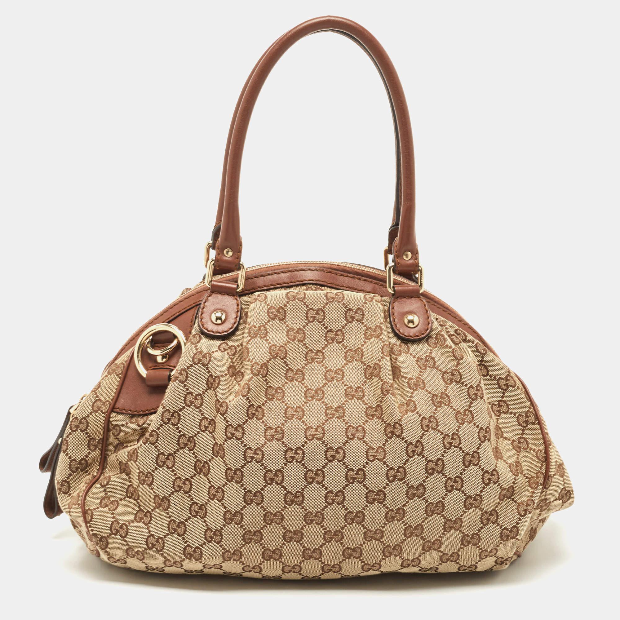 Die Sukey Boston Tasche aus dem Hause Gucci ist ein Klassiker. Die Tasche ist aus charakteristischem GG Canvas gefertigt und mit Lederbesätzen versehen. Sie ist mit einem geräumigen Innenraum aus Stoff und zwei Griffen ausgestattet.

