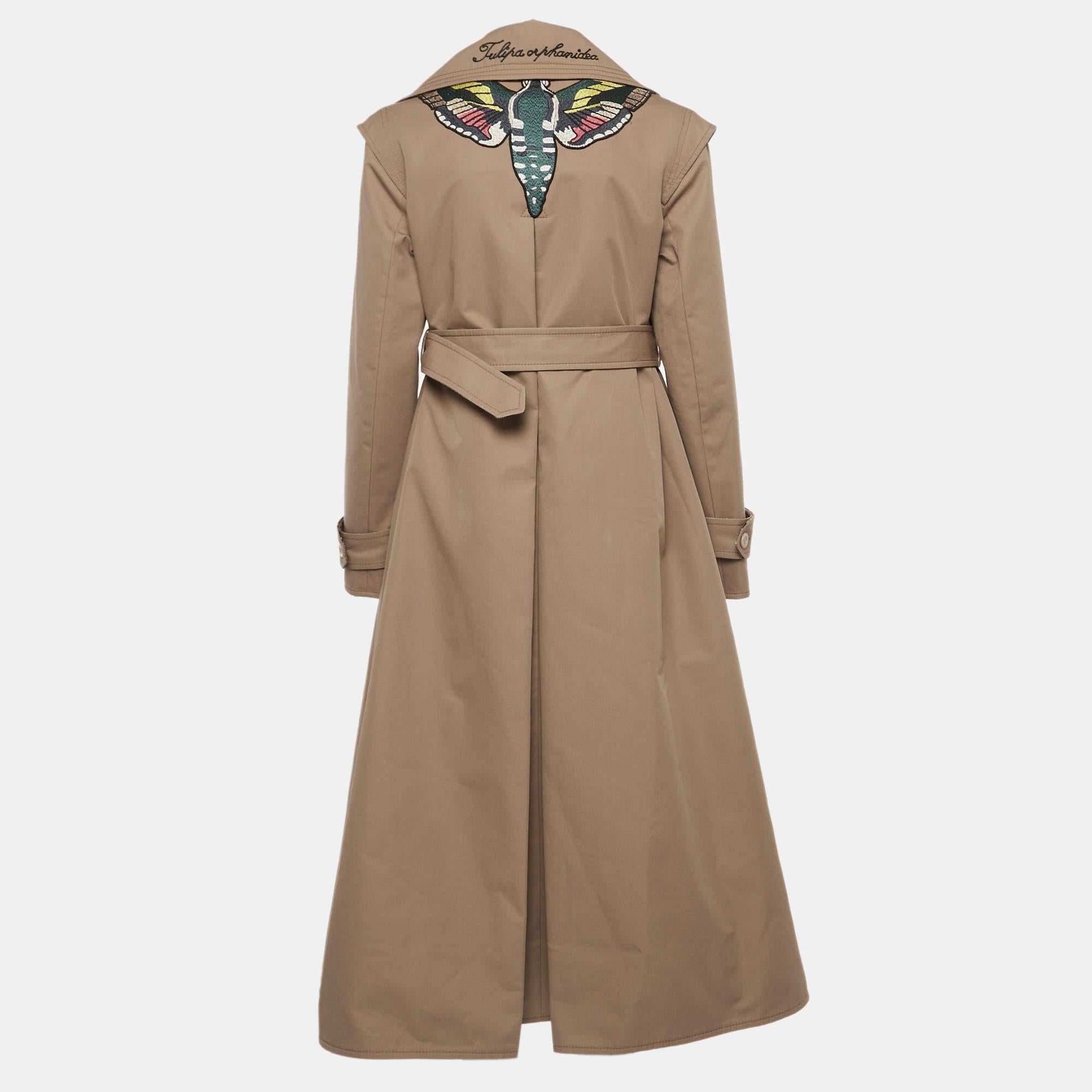 Der Trenchcoat von Gucci ist ein luxuriöses und ikonisches Kleidungsstück. Es ist aus hochwertigem Gabardine gefertigt und mit einer exquisiten Schmetterlingsstickerei auf der Rückseite versehen, die ihm einen skurrilen Touch verleiht. Der