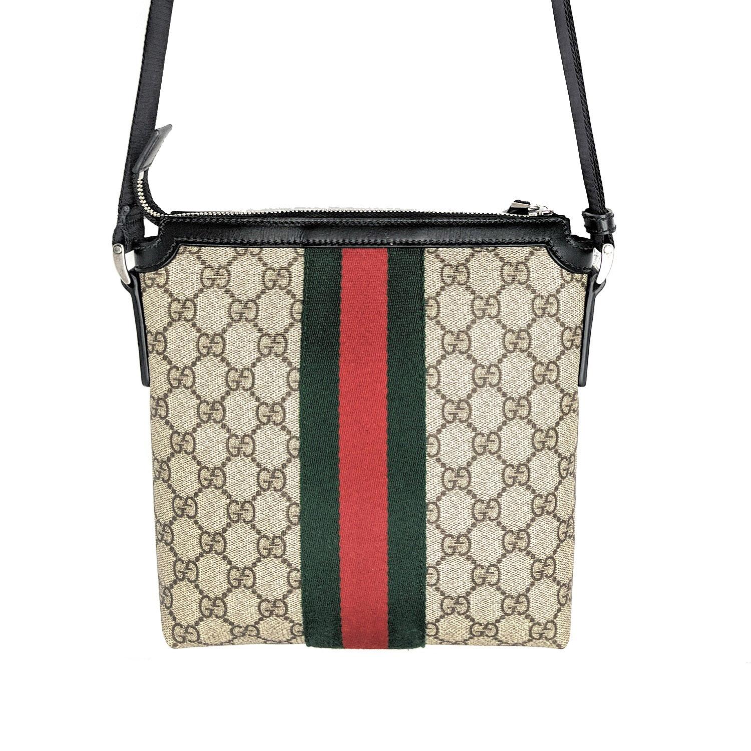 Coated canvas messenger bag in beige featuring logo pattern printed in brown. Buffed black leather trim throughout. Adjustable shoulder strap in black with leather strap pad. Leather logo appliqué at face. Signature striped web trim in green and red