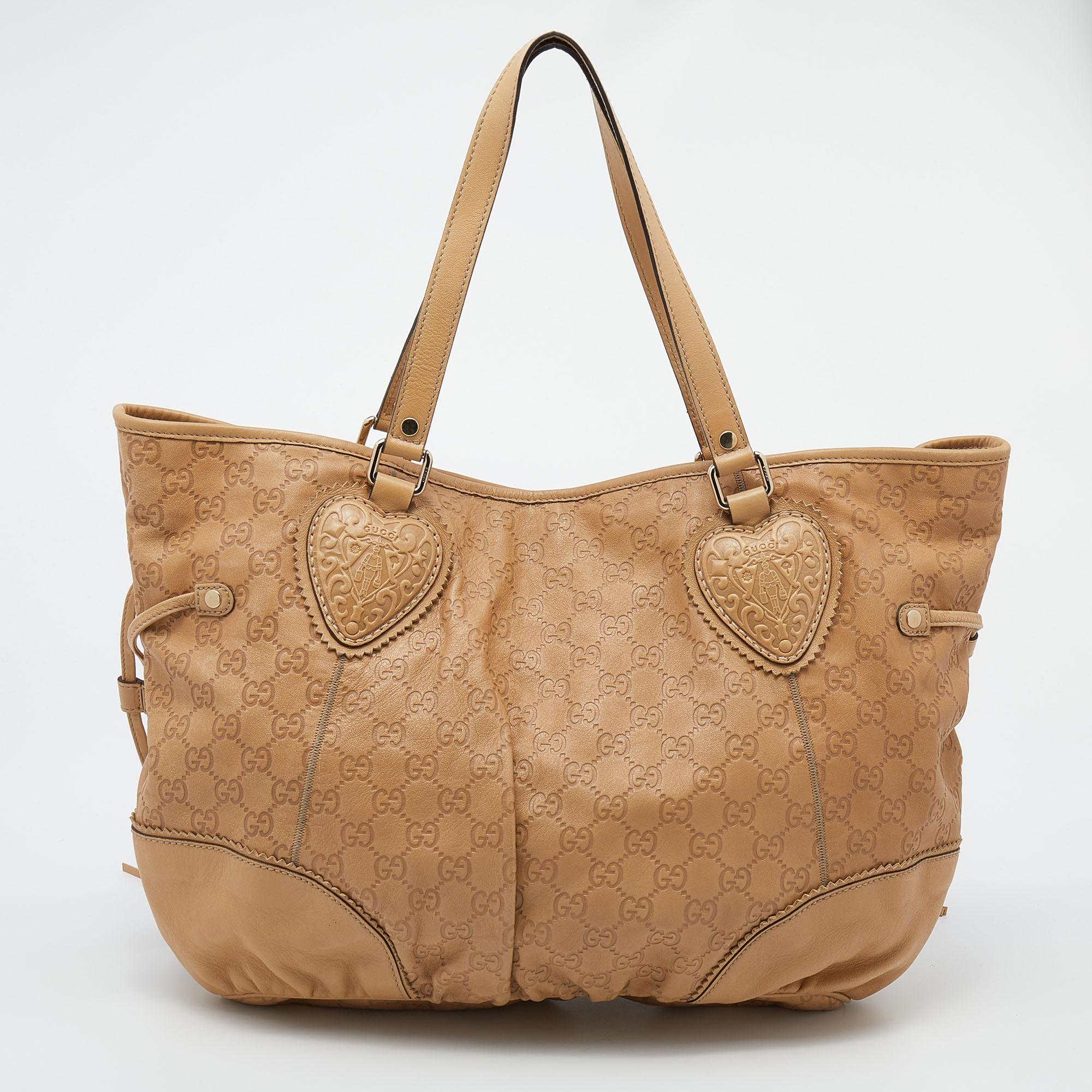 Great for everyday use, this Tribeca tote by Gucci is a wardrobe must! It is crafted from beige Guccissima leather trims. The everyday look is complete with heart pattern crests, fashionable side tassels, short leather handles, and gold-tone