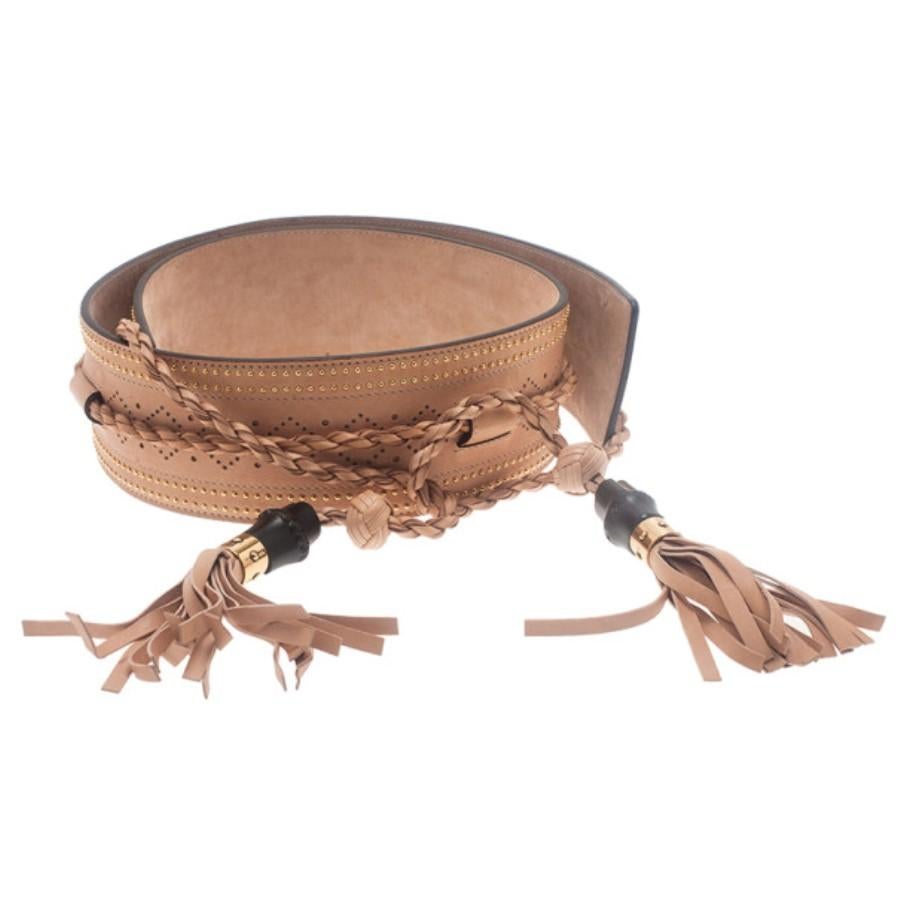 Take a dive into the fashion of the wild wild west with this Gucci belt. Made from leather, its sandy beige color is studded with golden studs along the sides and perforated with diamond-shapes patterns. The braided straps form tassels at the ends