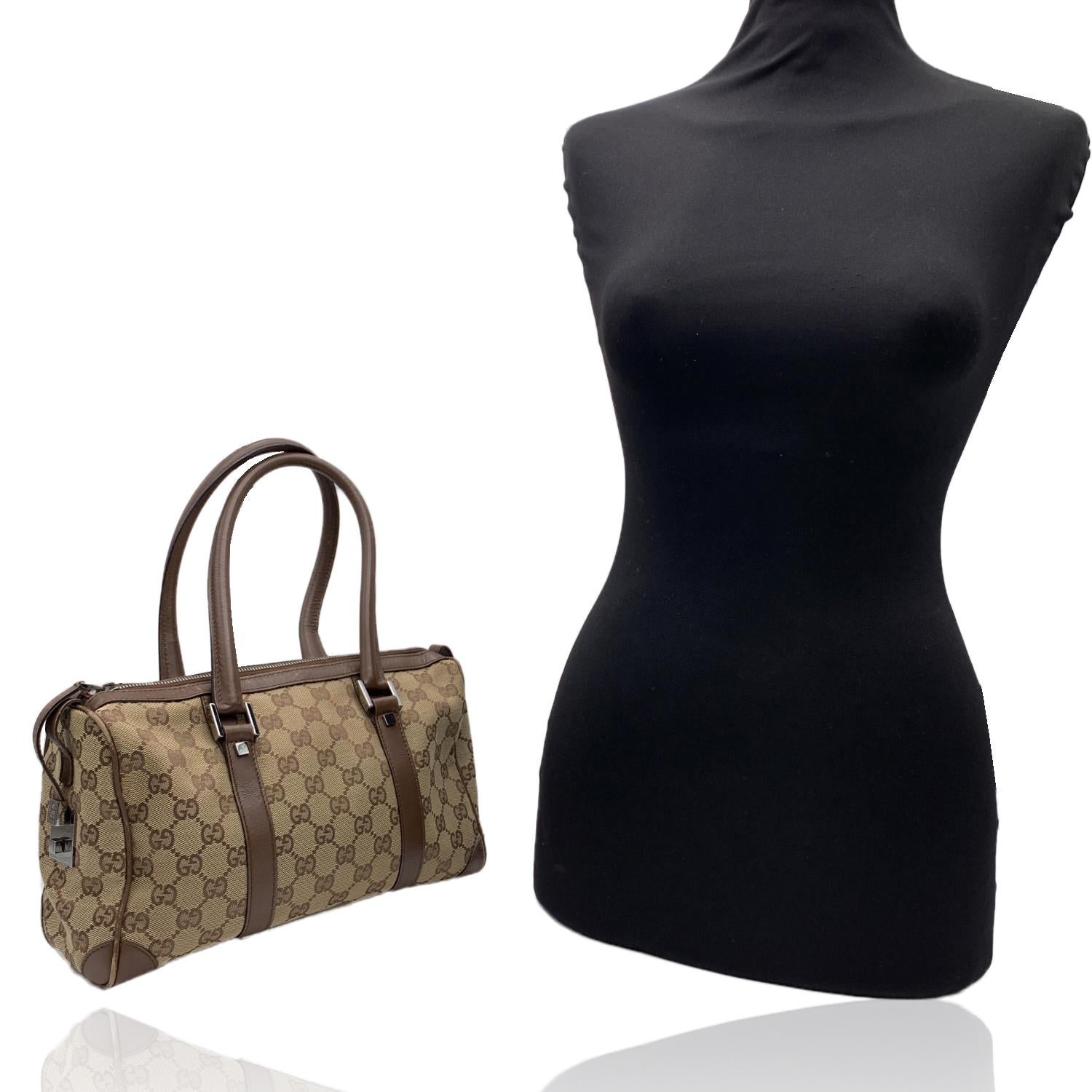 Monogram Boston Tasche von Gucci. Beigefarbenes Monogram Canvas mit braunem Echtlederbesatz und Griffen. Silberne Metallbeschläge Doppelte obere Griffe. Oberer Reißverschluss. Braunes Canvas-Futter. 1 Reißverschluss-Seitentasche innen. Etikett