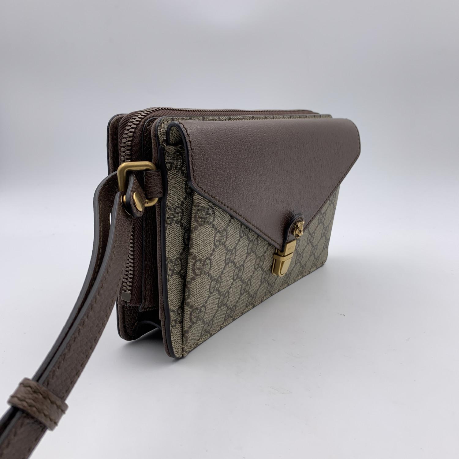 Gucci monogram canvas wrist bag. The bag is in GG supreme canvas with brown genuine leather trim and front flap. Gold metal tiger head on the front. 1 front flap pocket. Upper zipper closure. Beige microfiber lining. 2 interchangeable wrist straps