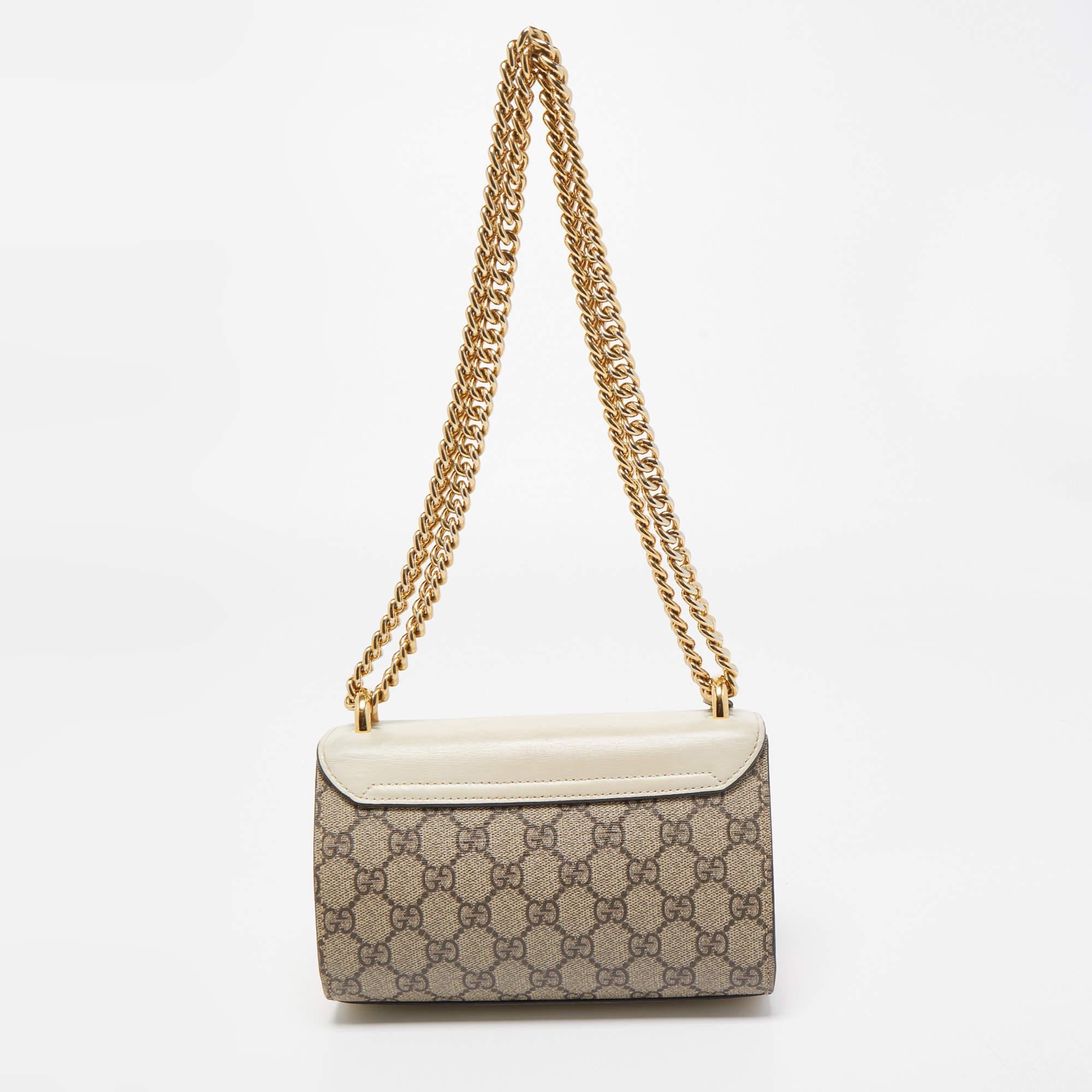 You'll surely fall in love with this spectacular shoulder bag from Gucci! The beige and off white bag is crafted from the signature GG Supreme canvas and leather into a structured silhouette. It flaunts a brand name engraved gold-tone padlock and