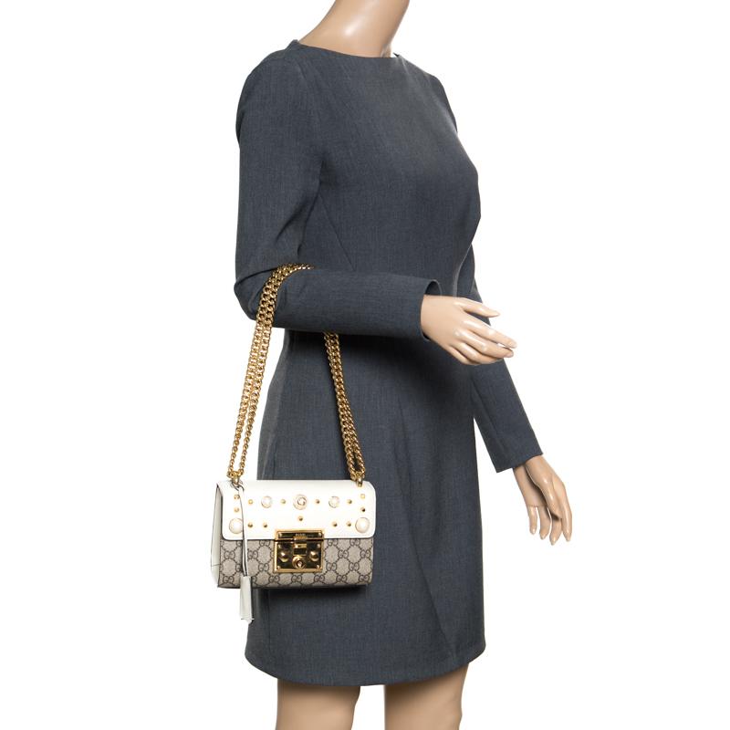 You'll surely fall in love with this spectacular shoulder bag from Gucci! The beige and off white bag is crafted from the signature GG Supreme canvas and features a front flap closure that is beautifully detailed with pearls and studs. It flaunts a