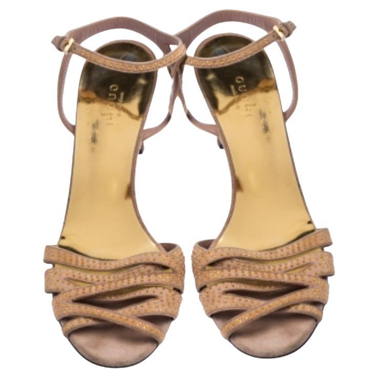 Complétez votre look élégant avec ces sandales Gucci. Confectionnée en daim beige, cette paire présente des brides cloutées dorées sur le devant, des brides bouclées à la cheville et une semelle intérieure confortable doublée de cuir. Cette jolie