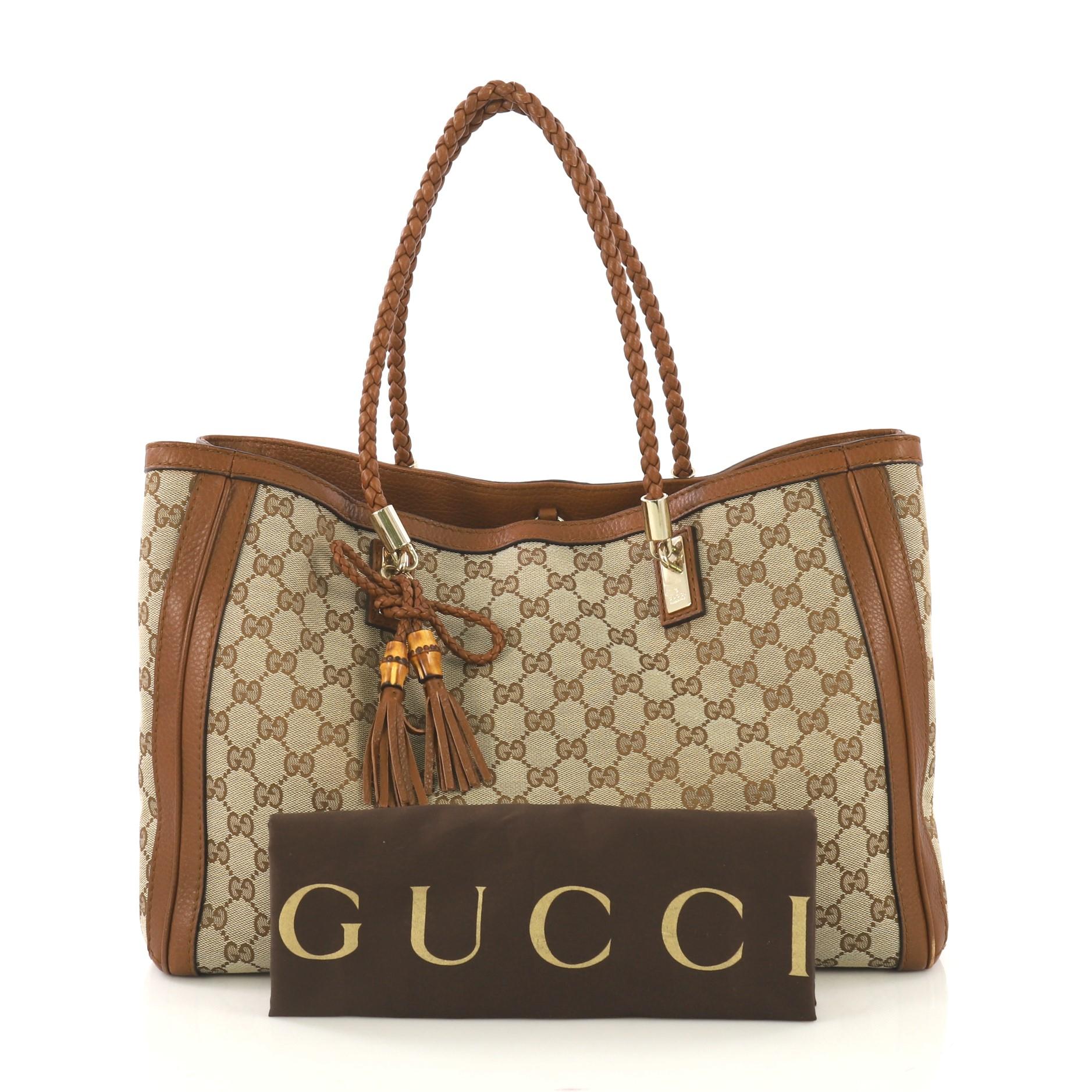 This Gucci Bella Tote GG Canvas Medium, crafted from brown GG canvas, features dual braided leather handles, protective base studs, leather trim, and gold-tone hardware. Its hook closure opens to a beige fabric interior divided into two compartments