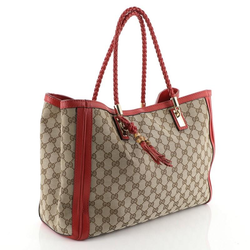 This Gucci Bella Tote GG Canvas Medium, crafted from brown GG canvas, features dual braided leather handles, protective base studs, leather trim, and gold-tone hardware. Its hook closure opens to a neutral fabric interior divided into two