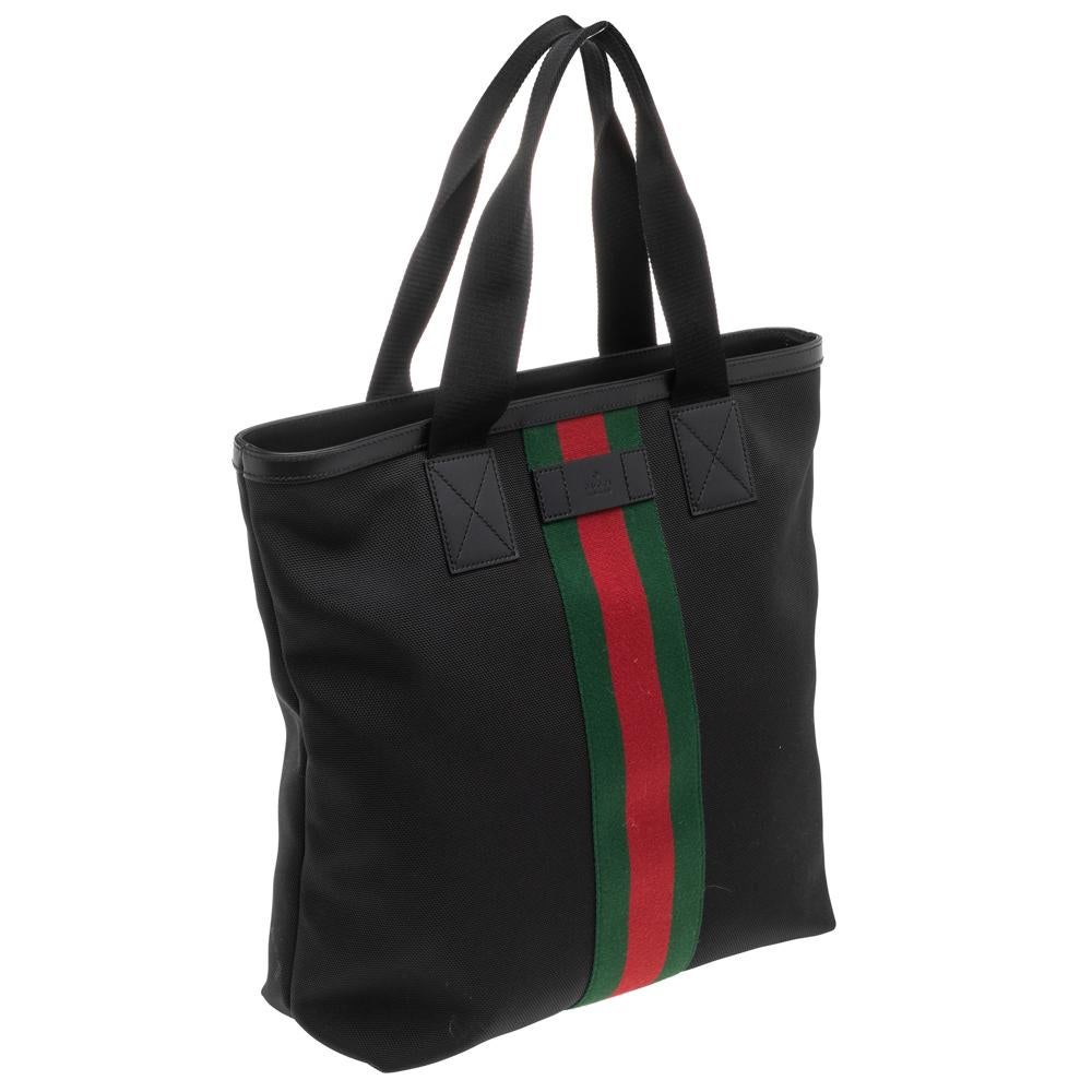 This classic Gucci tote is casual and fun! Crafted from black canvas, it has signature Web detailing on the exterior and the brand label at the front. It comes with two top handles and top zip closure. Its interior is lined with nylon and houses a