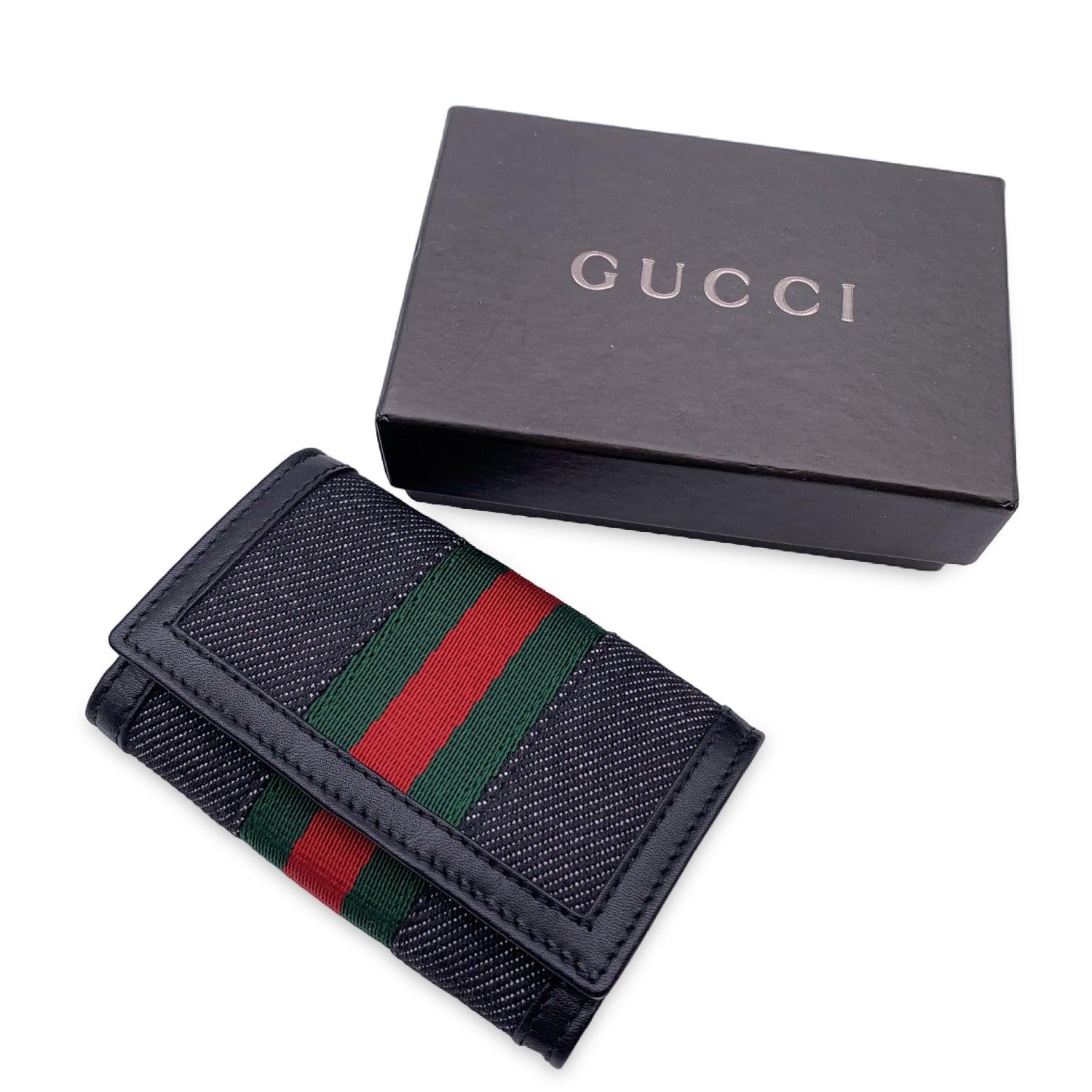 Key case in black denim canvas by Gucci. Green/Red/Green striped detailing. Snap closure on the front. Leather lining. Silver metal hardware. 6 key rings inside. 'Gucci - Made in Italy' embossed inside. Details MATERIAL: Cloth COLOR: Grey MODEL: