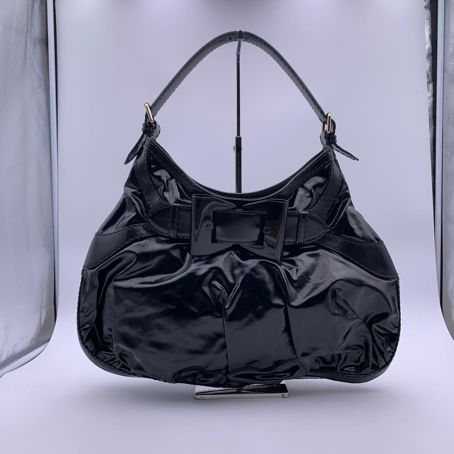 Gucci 'Queen' Hobo bag, crafted from black coated canvas with black leather trim. Oversized bow lucite buckle on the front. Single loop leather handle. Gold tone hardware. Magnetic button closure on top. Gucci signature lining. 1 side zip pocket & 2