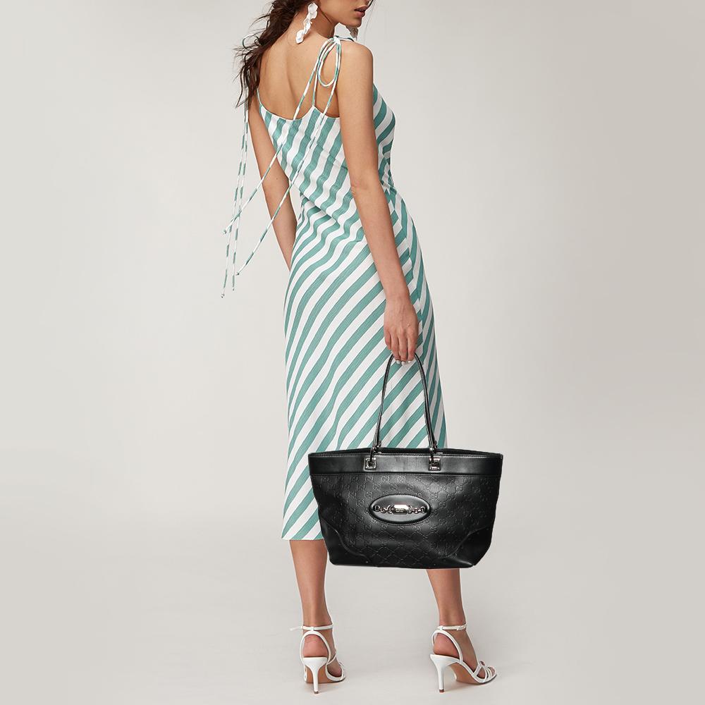 Your search for that perfect everyday tote ends here. Glide from day to night with this Gucci Guccissima leather tote that offers a spacious design. This classic black bag is complete with dual top handles and a metal logo accent at the