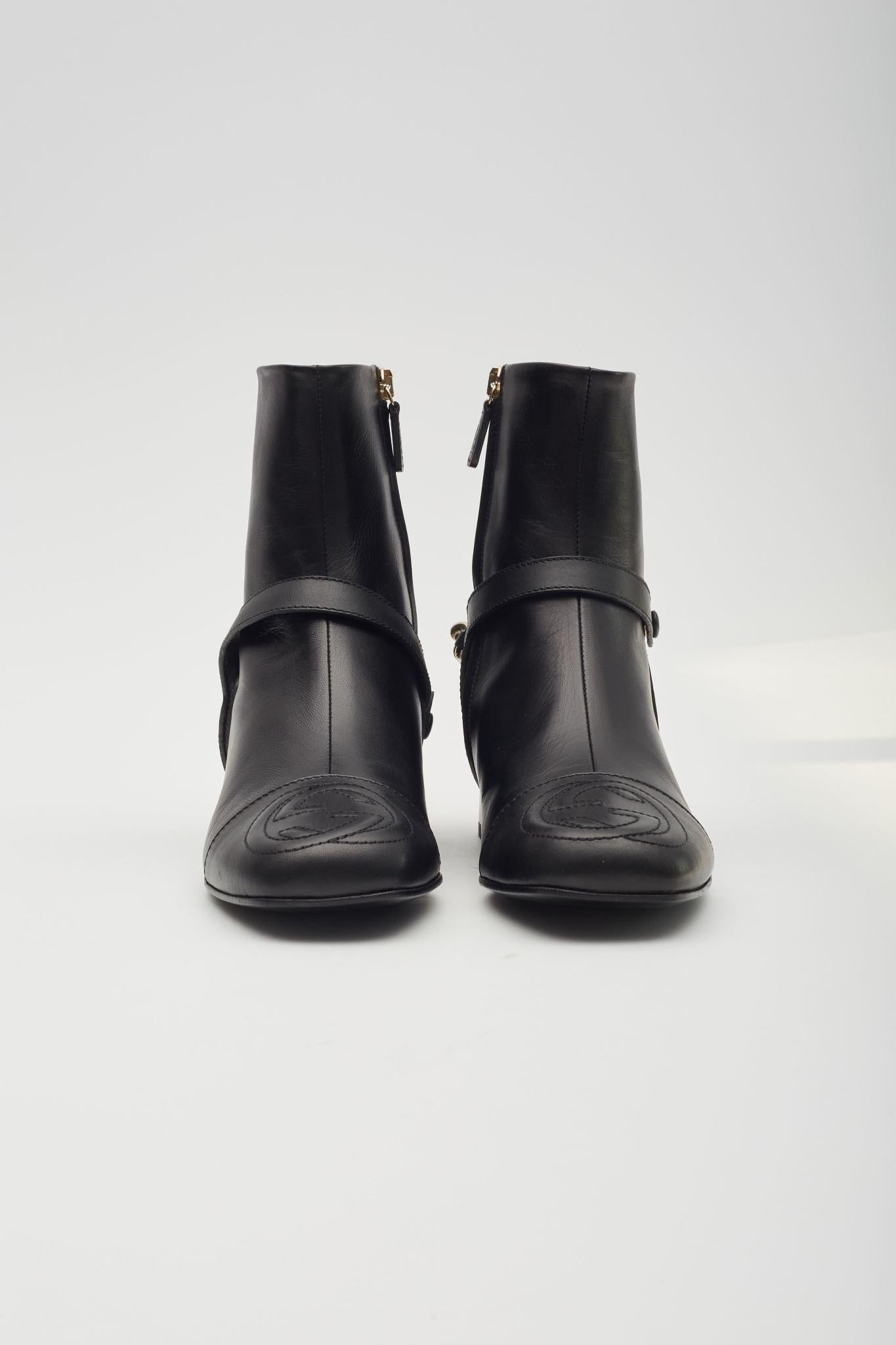 Ces bottes tombent juste au-dessus de la cheville et sont fabriquées en cuir de veau noir. Elles sont dotées d'un talon de 2,5 cm, d'une chaîne en or léger à l'arrière de la cheville et d'un logo GG entrelacé sur le bout du pied carré.