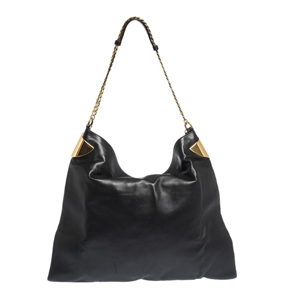 Picked from Gucci's 1970 collection, this black leather shoulder bag has a top with metal accents on the sides, a gold-tone chain that holds the bag and a well-sized canvas interior secured by a snap button. It is finished with a gorgeous tassel