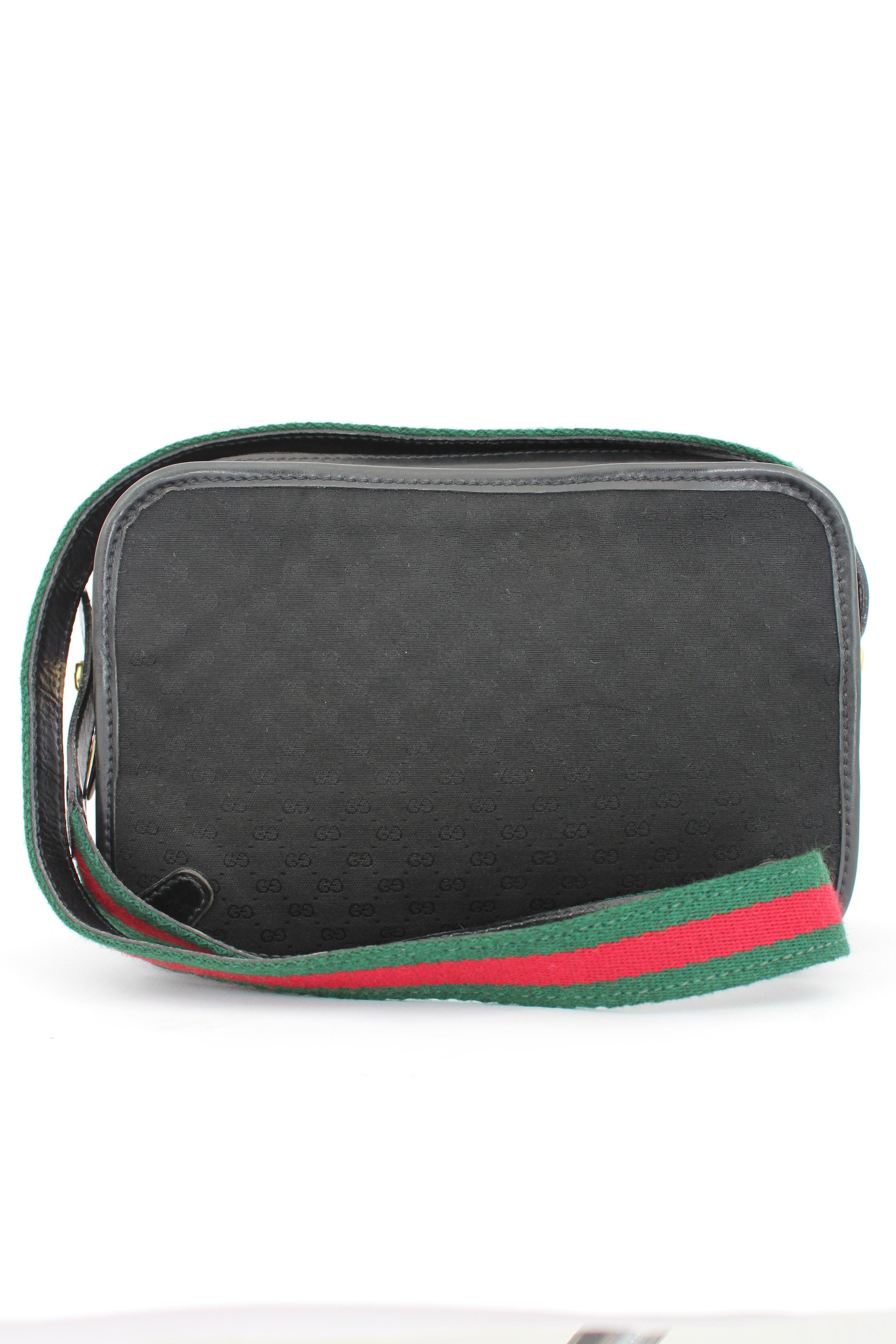 Gucci vintage 80s shoulder bag. Camera bag model, black color and gold-colored details. Tone-on-tone monogram pattern. Green and red shoulder strap, typical colors of the fashion house. Bag with three compartments, each closed by branded zippers.