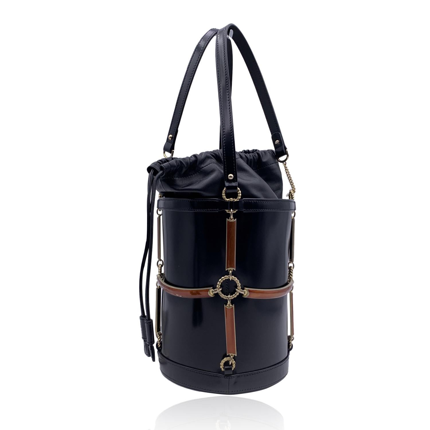 GUCCI Enamel Mini Bucket Bag in black leather from the 2018 collection. The bag features a decorative gold metal cage accented with tan enamel. The bag features double handles and upper drawstring closure. It opens to a grey floral printed fabric