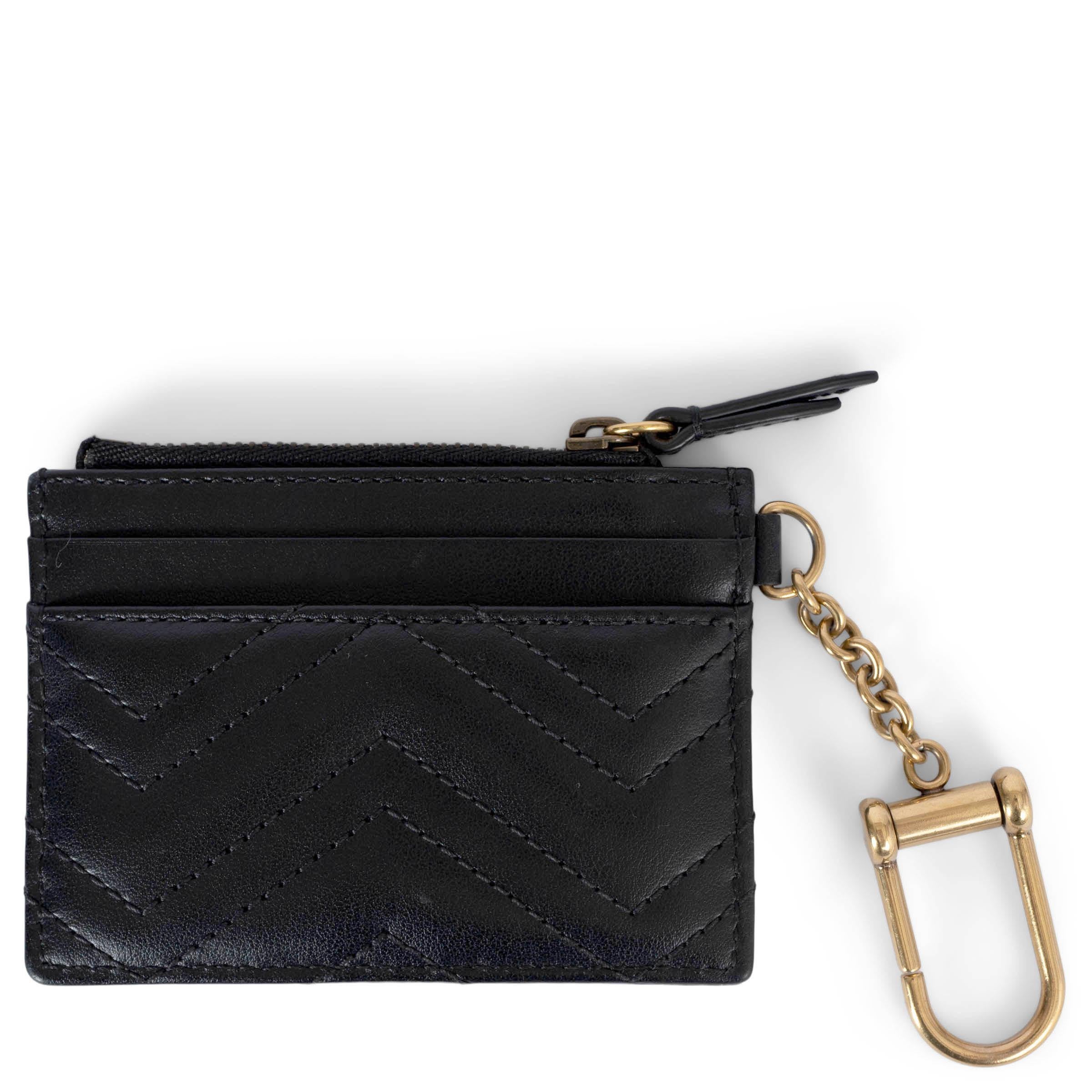 Esta cartera llavero Gucci GG Marmont 100% auténtica está confeccionada en piel chevron matelassé negra y acentuada con herrajes dorados envejecidos. Cuenta con un bolsillo con cremallera, cuatro ranuras para tarjetas de crédito y un llavero con