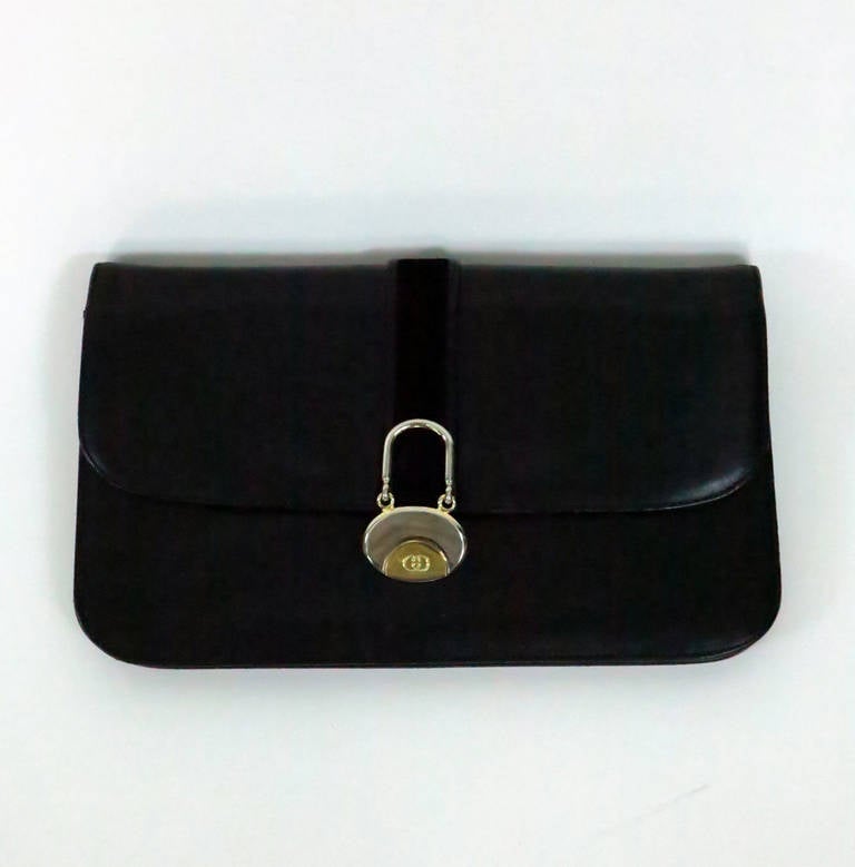 Vintage Gucci black leather clutch. Flap bag has decorative black suede strip with Gucci logo tab in gold & silver. Center zipper compartment (lined in taffeta) inside with two open leather lined compartments on either side. In very good condition,