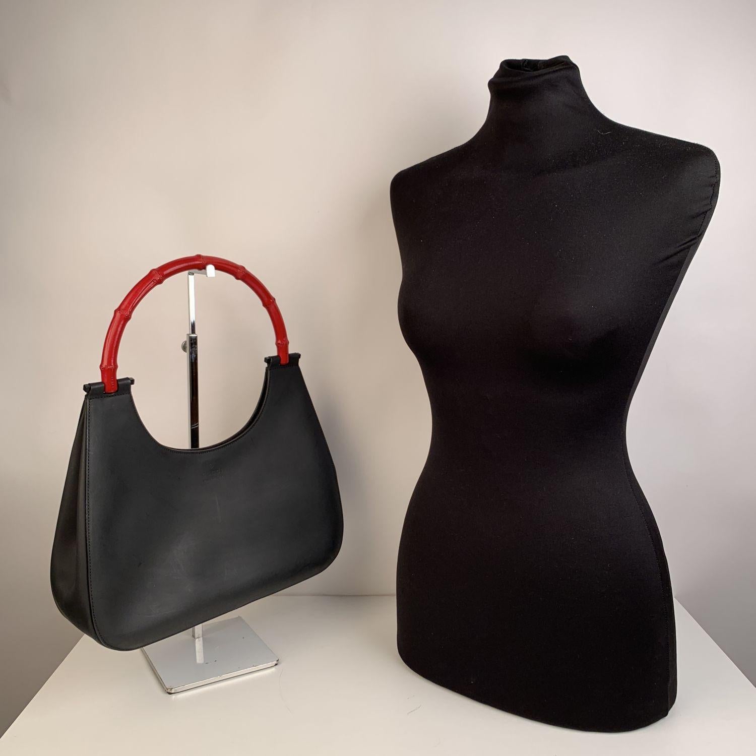 Beautiful Gucci hobo bag, crafted in black leather with bambbo handle, painted in red color. The bag features the 'Gucci - Made in Italy' writing engraved on the front, a magnetic button closure on top, suede lining with and 1 side interior zip