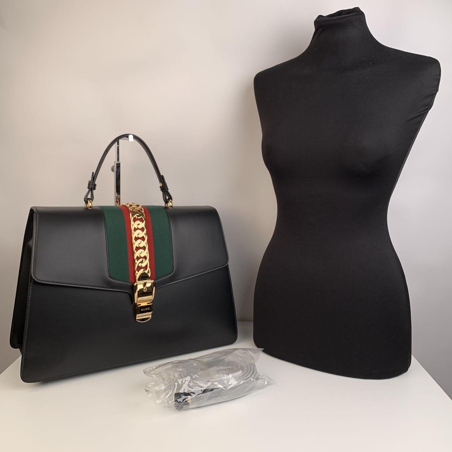 Stunning maxi 'Sylvie' top handle bag by Gucci. This is the larger versione of the Sylvie satchel line, now discontinued. It is crafted in smooth black calfskin leather with iconic green/red/green signature web detail and gold metal chuncky chain on
