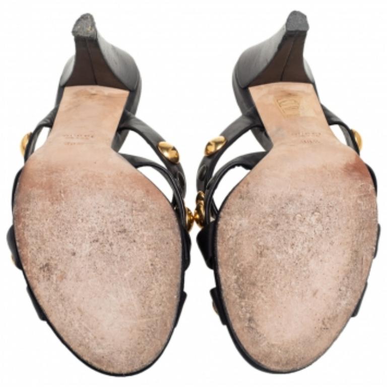 Questi sandali di Gucci sono semplicemente stupendi! Sono realizzate in pelle nera con un design di cinturini incrociati e abbellimenti dorati, con punte aperte, tacco di 10 cm e solette confortevoli.