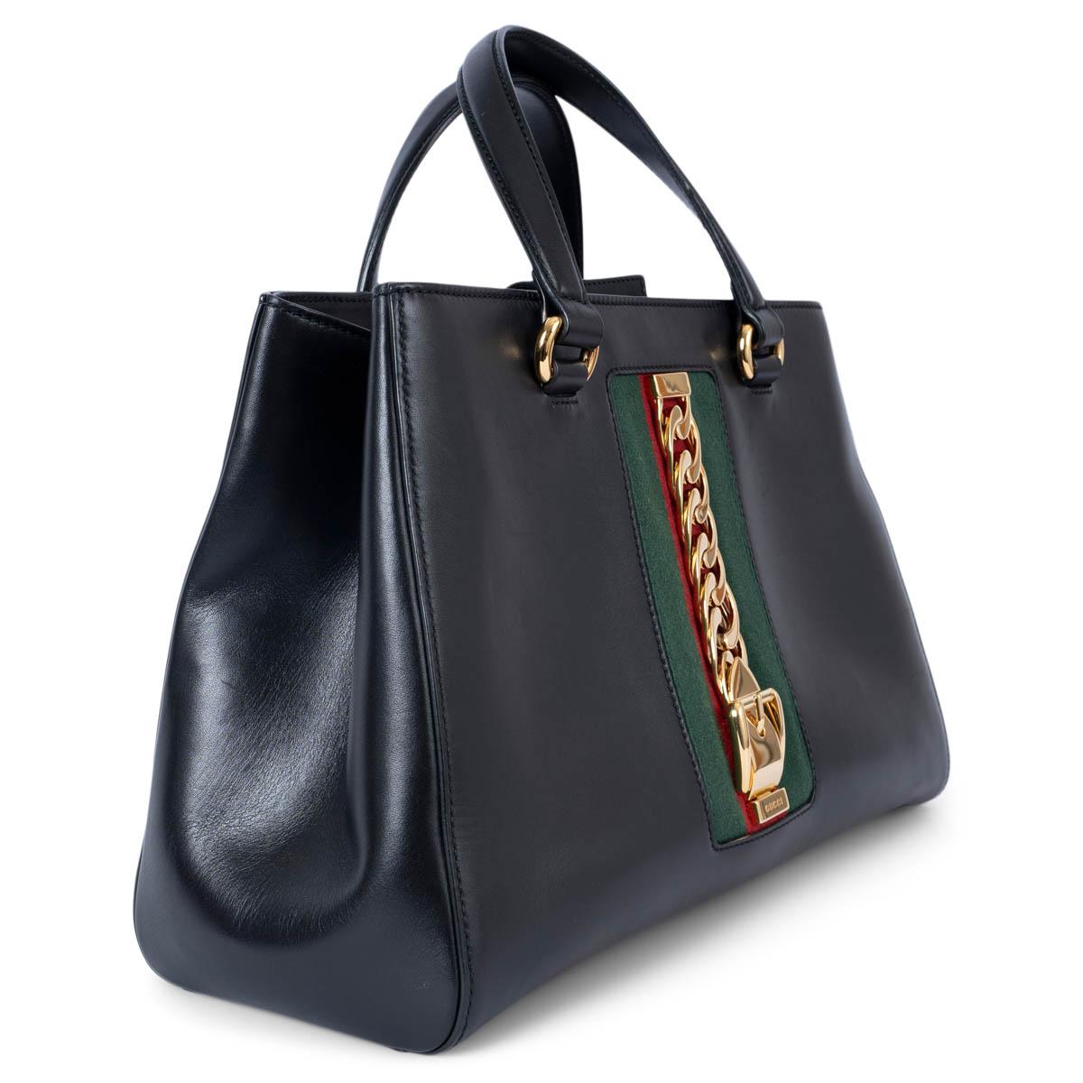 100% authentic Gucci Large Sylvie top handle tote bag in smooth black leather with green and red classic Web on the front embellished with gold-tone metal buckle chain detail. Opens with a magnetic button and is lined in beige suede with a large