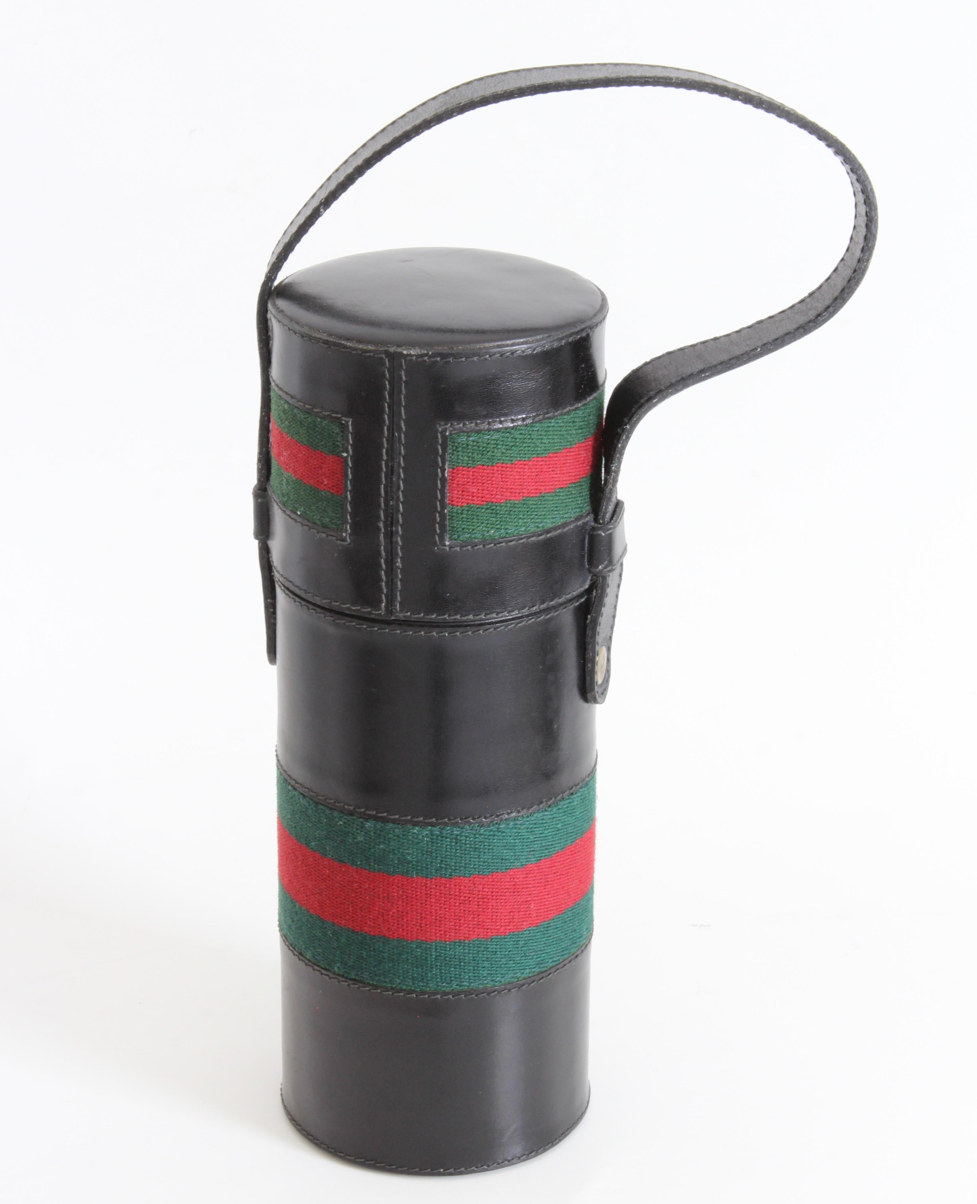 This incredibly rare leather tote with insulated bottle was made by Gucci, most likely in the early 1970s. 

The cover is made from black leather and features Gucci's iconic red and green webbing at the center.  It opens to reveal a steel flask with