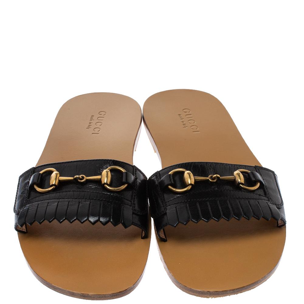 Diese hübschen Slide-Sandalen sind genau die richtige Wahl für einen entspannten Tag im Freien. Die Flats sind aus schwarzem Leder gefertigt und mit Fransendetails und dem charakteristischen Horsebit-Motiv aus goldfarbenem Metall auf dem vorderen