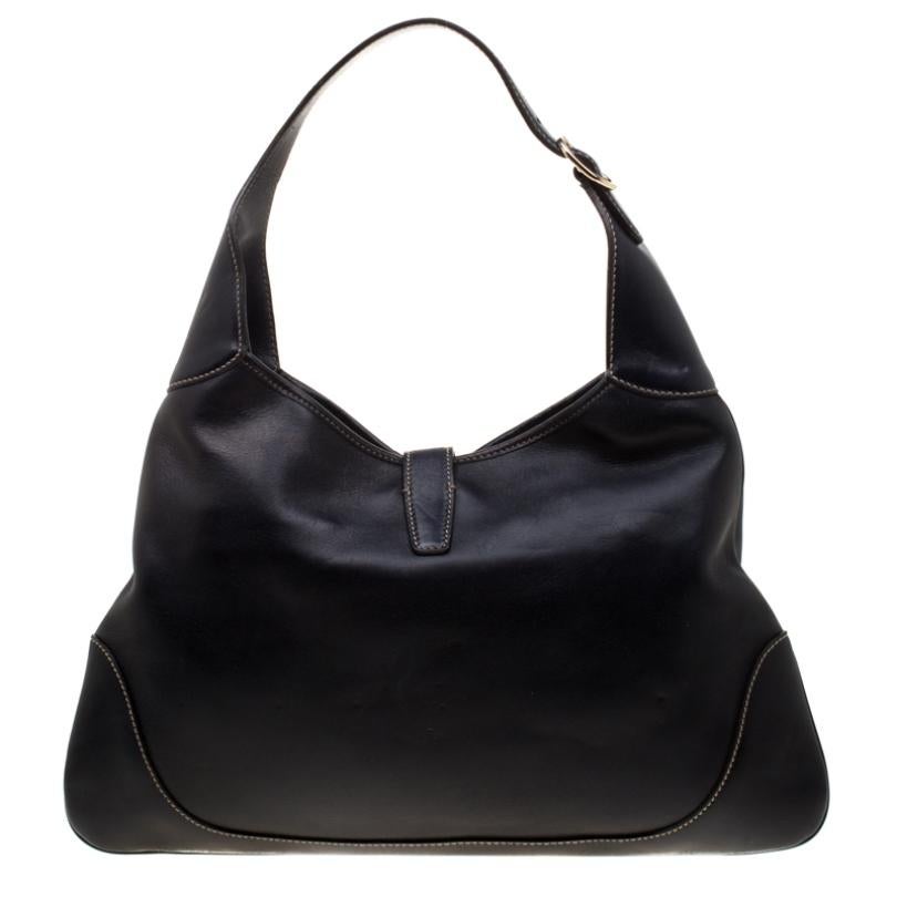 Get a modern yet classic look with this black leather Gucci Jackie O hobo. The front features gorgeous the signature web detail on the middle, and unique hook closure in gold-tone connected to a small leather flap. The bag also has an adjustable