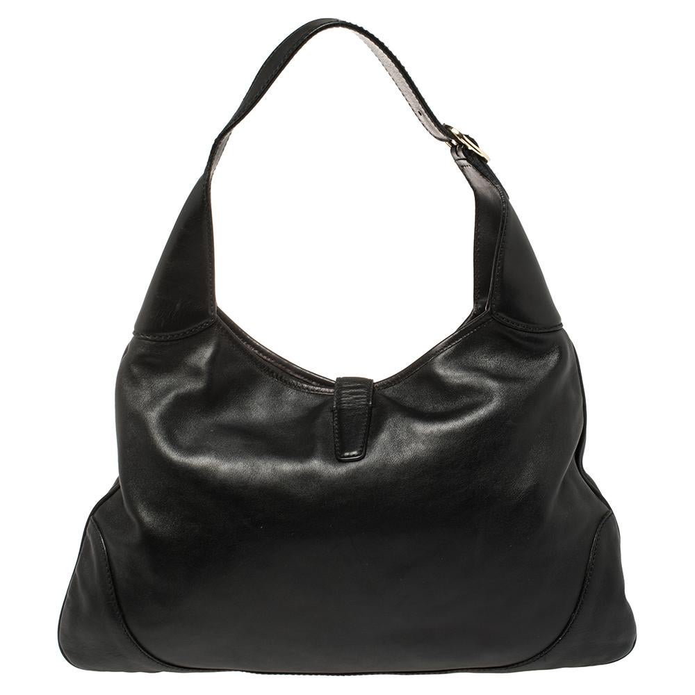 Get a modern and classy look with this black leather Gucci Jackie O hobo. The front features the signature web detail on the middle-front and piston push-lock closure in gold-tone connected to a small leather flap. The bag also has an adjustable