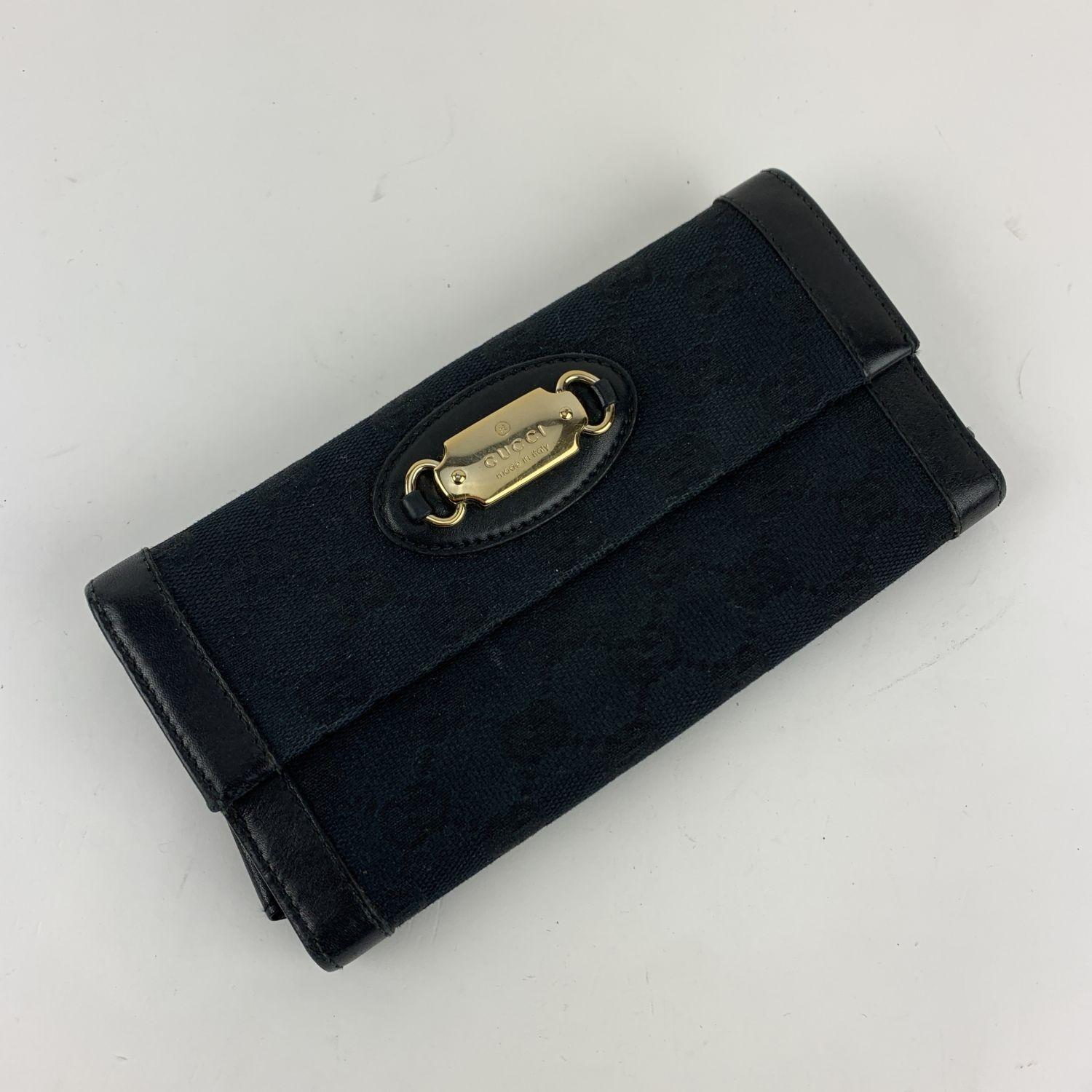 GUCCI black continental 'Punch' wallet in monogram canvas and leather. Flap with button closure on the front. Gold metal Gucci plate on the front. Fold over strap with button closure on the back. 7 credit card slots, 1 bill compartment and 2 open