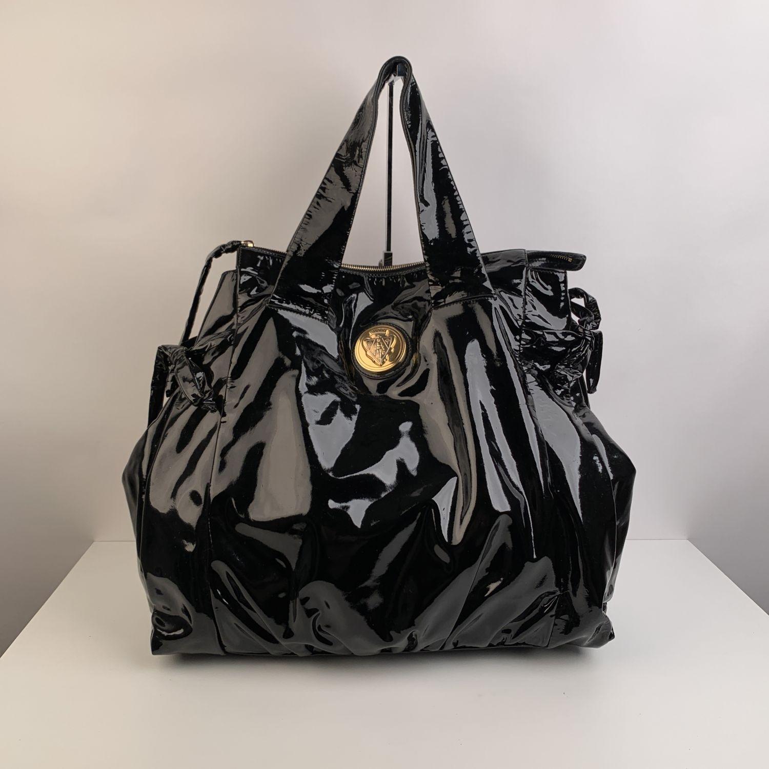 Gucci black patent leather Hysteria tote handbag. GUCCI crest round plaque on the front. Gold-tone hardware. Side self-tie details. Dual flat leather top handles (4