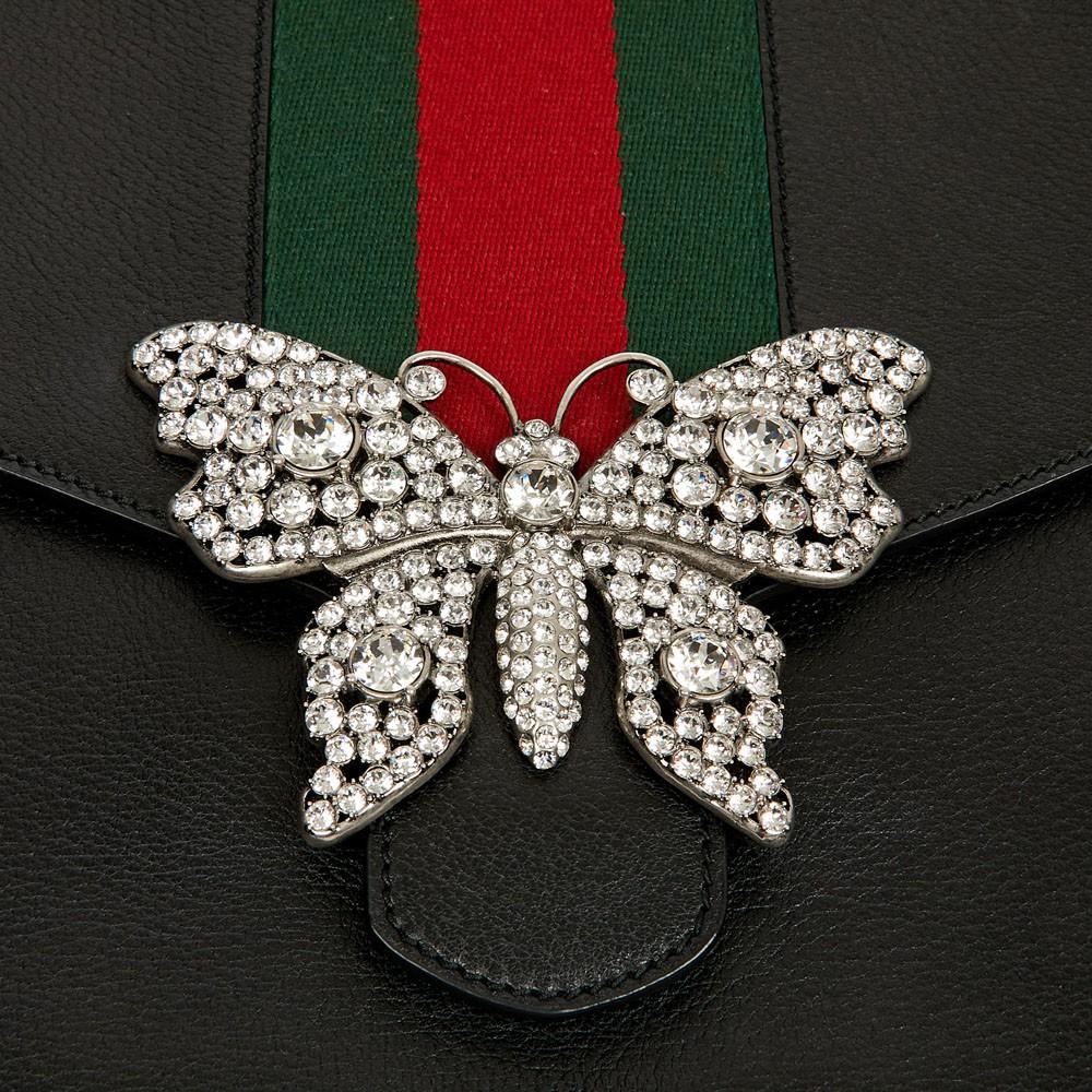Gucci black leather pouch. 
Alessandro Michele, Artistic Director of the House of Gucci since 2015, imagined this black grained leather clutch bag embellished with a large butterfly brooch made of silvery metal and crystals. 
In the center of the