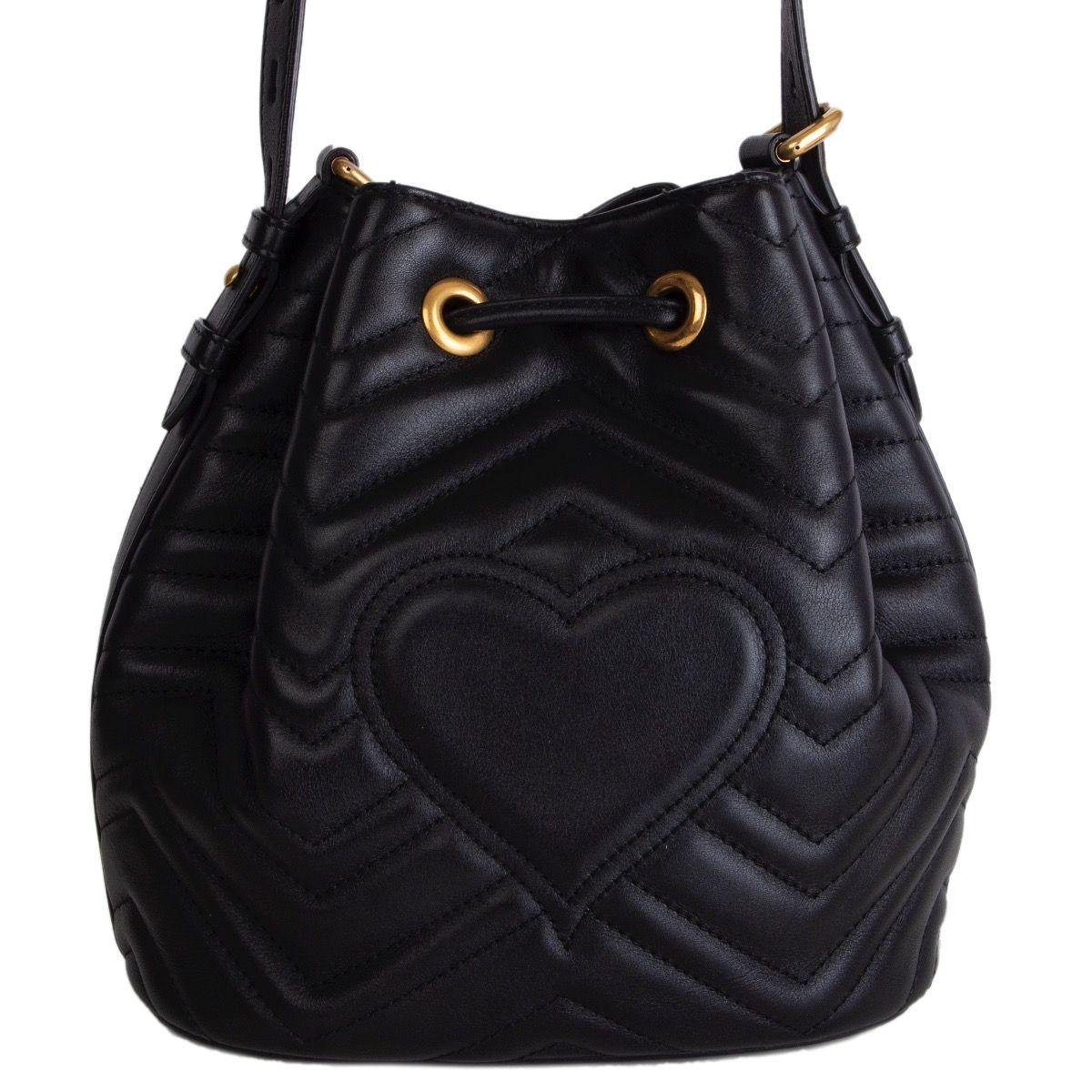 Gucci GG Marmont Matelasse bucket bag in black quilted leather with detachable leather strap and striped web strap. Closes with a drawstring on top. Lined in pink suede with an open pocket against the front and back. Has been carried and is in