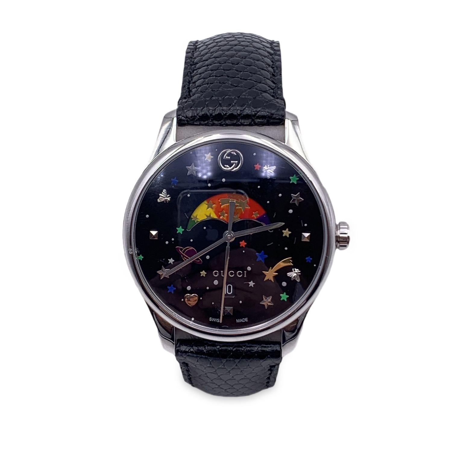 Gucci 'G-Timeless - Moonphase' stainless steel unisex watch. Model 126.4. Round steainless steel metal case (38 mm - crown included). Black dial with date function. This watch features multicolored bee, stars and planets motif. Ronda quartz