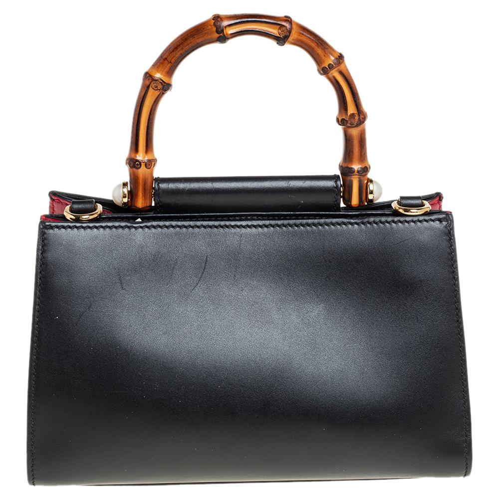 This Gucci Nymphaea bag is characterized by recognizable bamboo handles and an elegant silhouette. Crafted in smooth, black leather, this bag boasts a spacious interior lined with Alcantara and is equipped with an additional shoulder strap. A